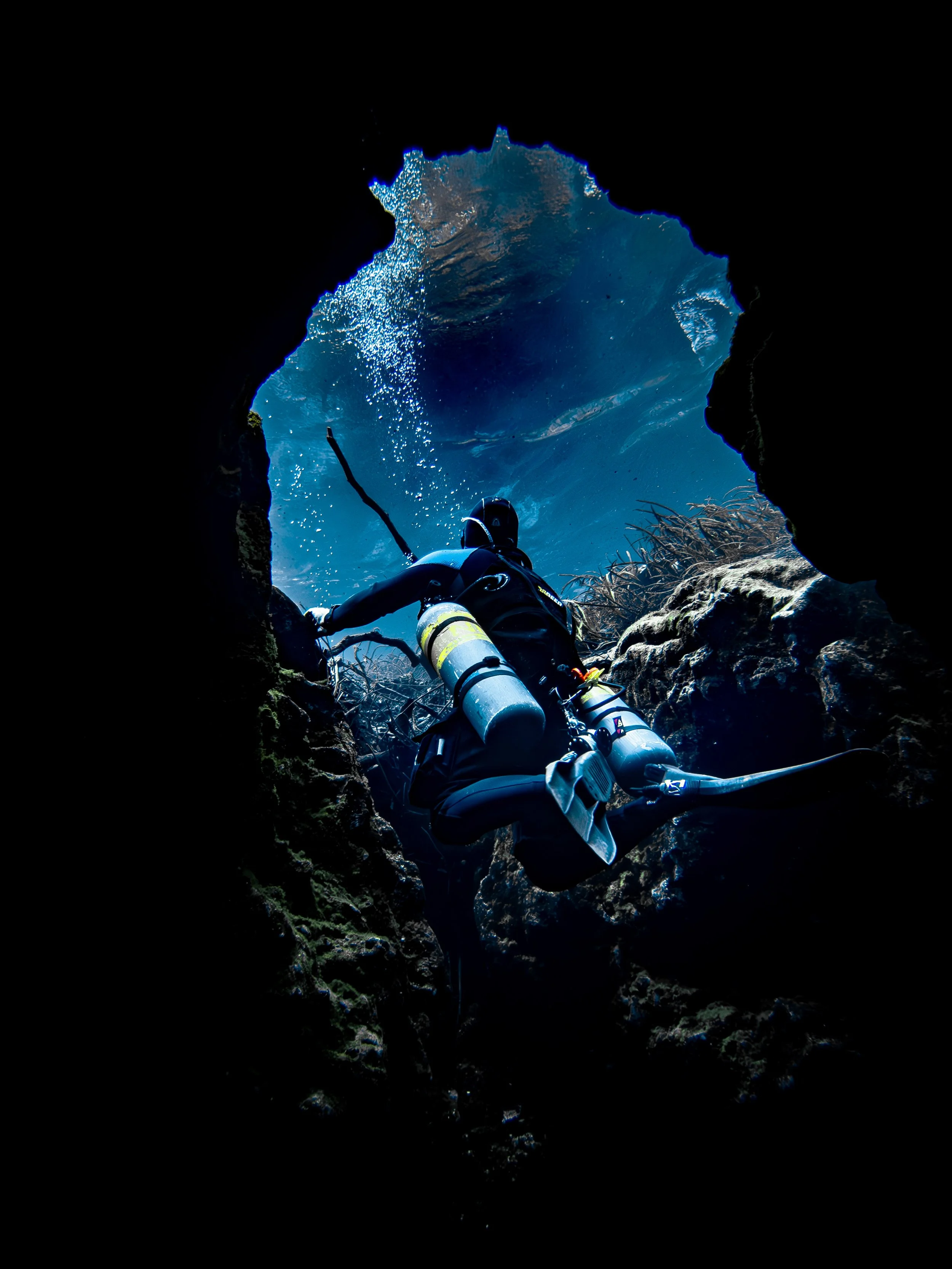 A scuba diver exploring an underwater cave with a view of the water from inside the cave.