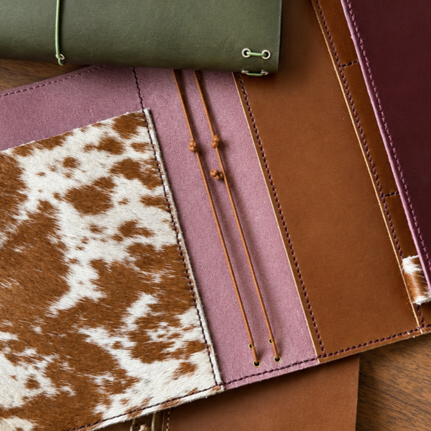 Close-up of leather and fabric swatches, including a cowhide pattern, in various colors like green, pink, brown, and purple, arranged on a wooden surface.