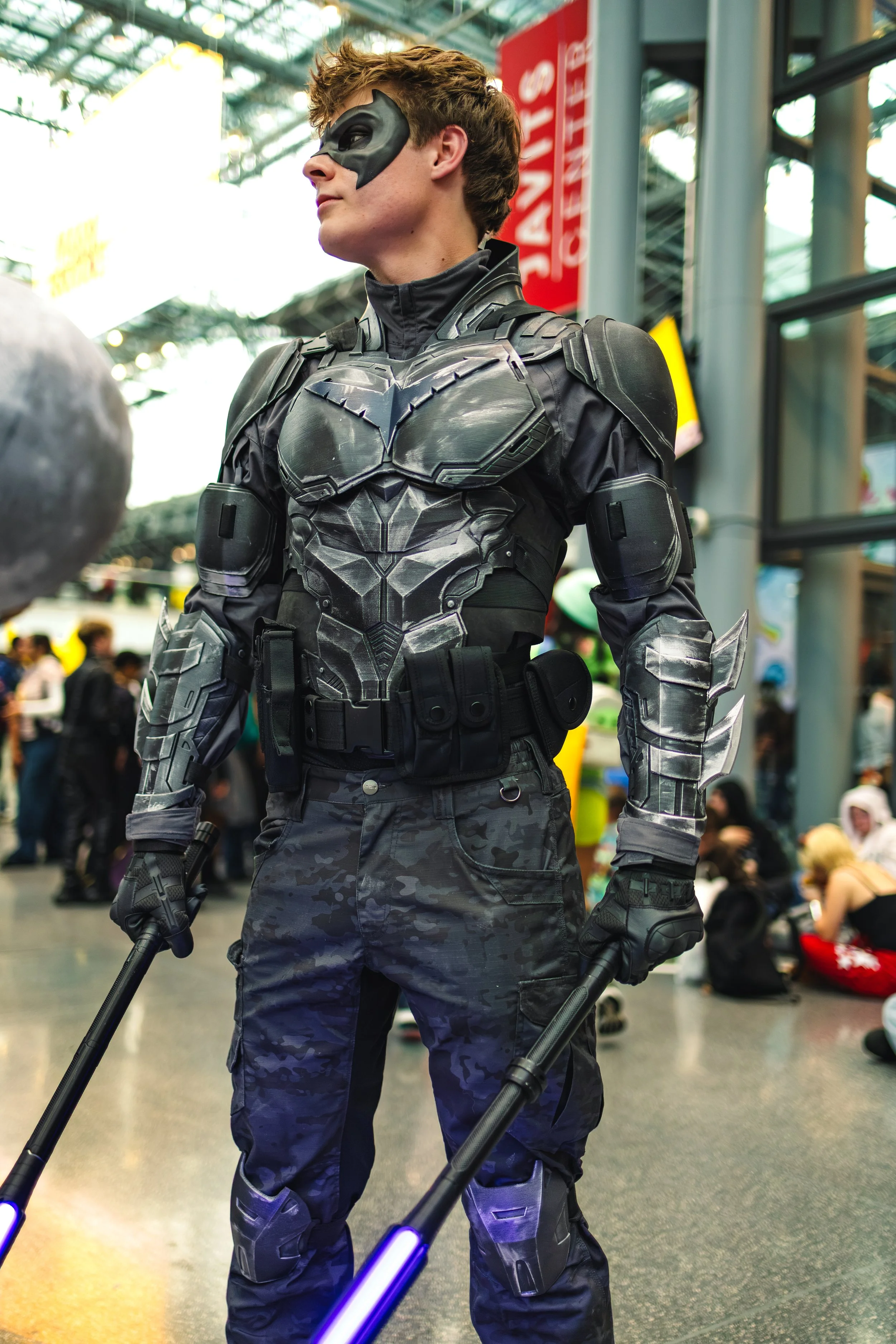 Person dressed as Batman in a futuristic battle suit at a convention, holding weapons in both hands.