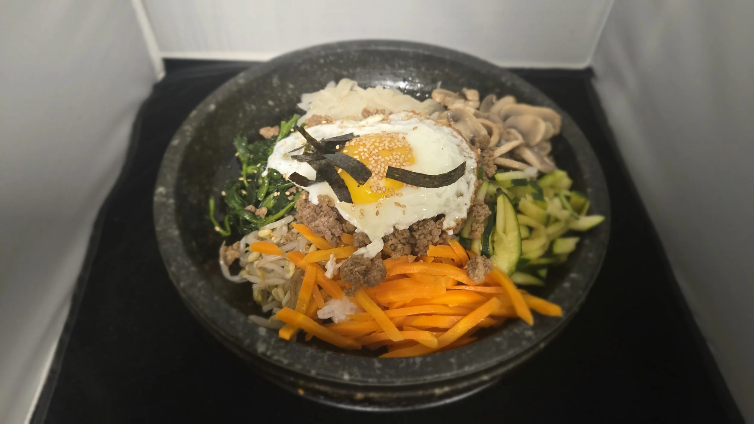 Korean bibimbap dish with vegetables, ground beef, a fried egg, and seaweed strips served in a hot stone bowl.