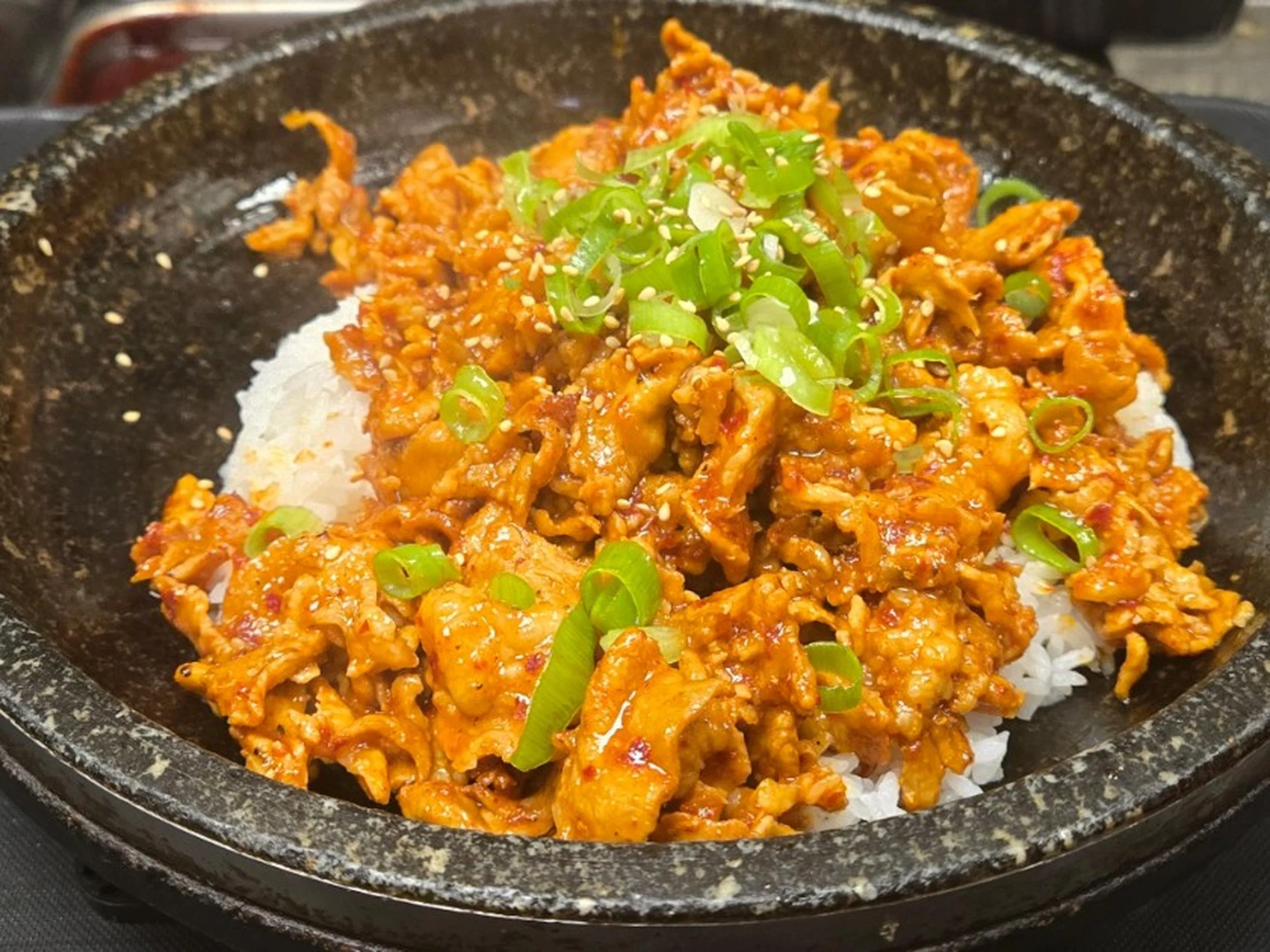 A cast iron skillet containing cooked Asian-inspired ground meat dish garnished with sliced green onions and sesame seeds, served over white rice.
