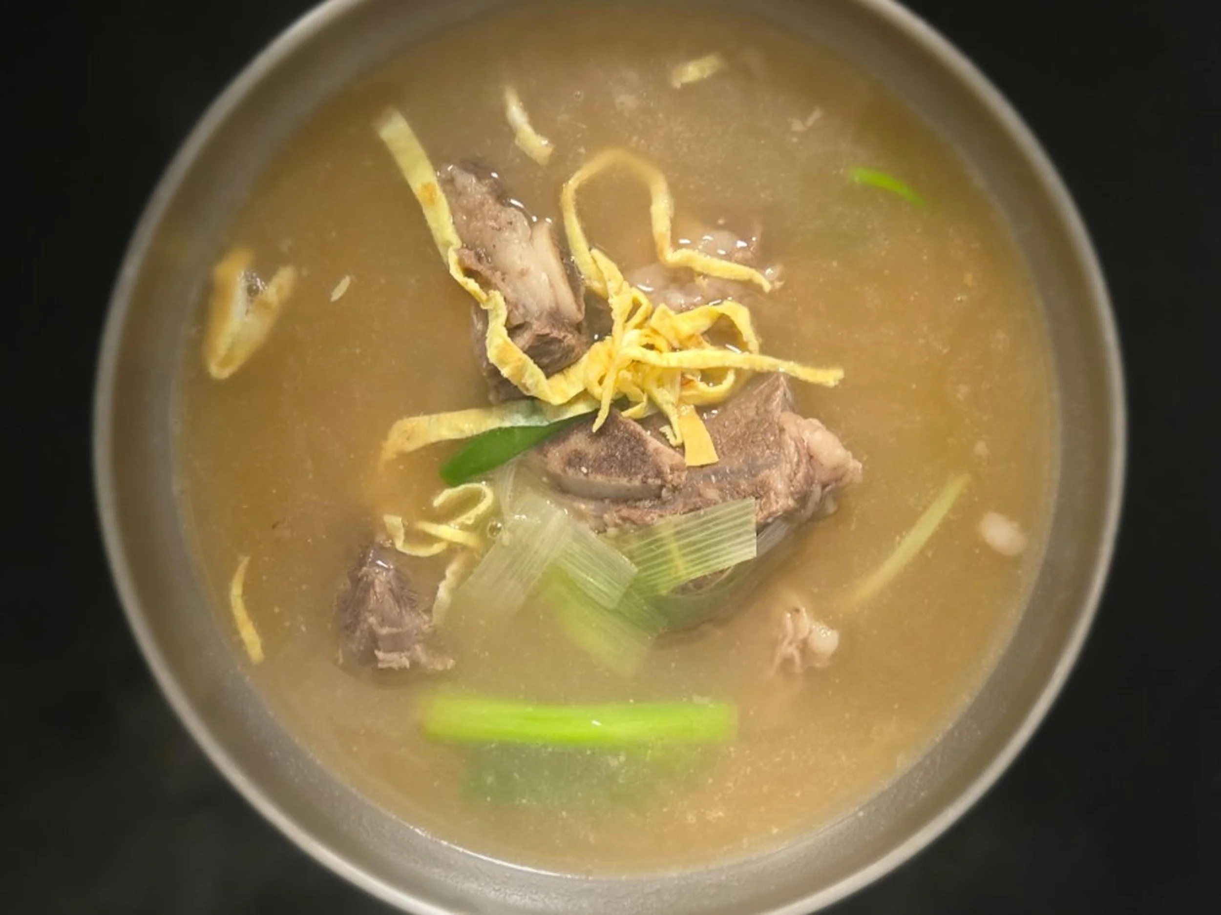 A bowl of soup with visible pieces of beef, shredded egg, and green vegetables in a clear broth.