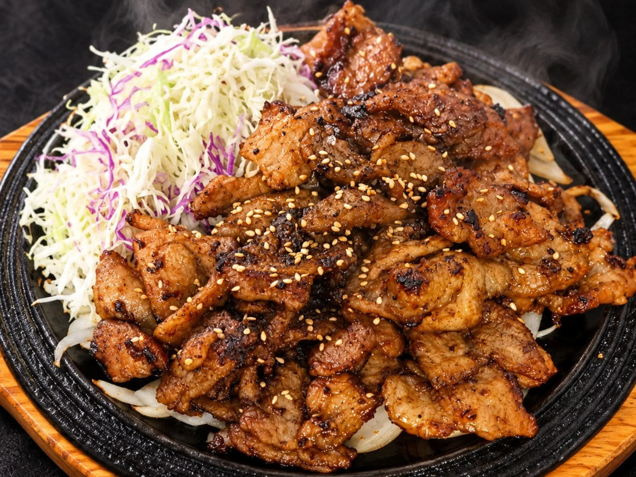 Grilled meat with sesame seeds served on a sizzling hot plate with shredded cabbage and lettuce on the side.