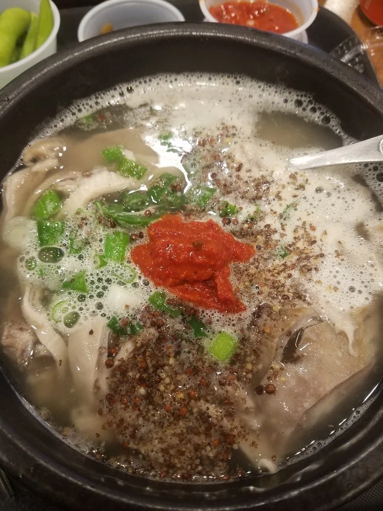 A bowl of hot soup containing green onions, red chili paste, black pepper, and other ingredients.