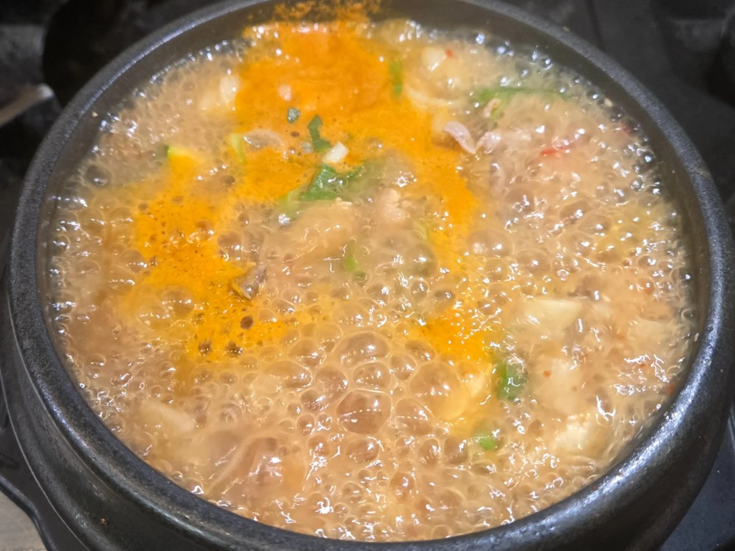 A pot of bubbling soup with orange and green herbs or vegetables.
