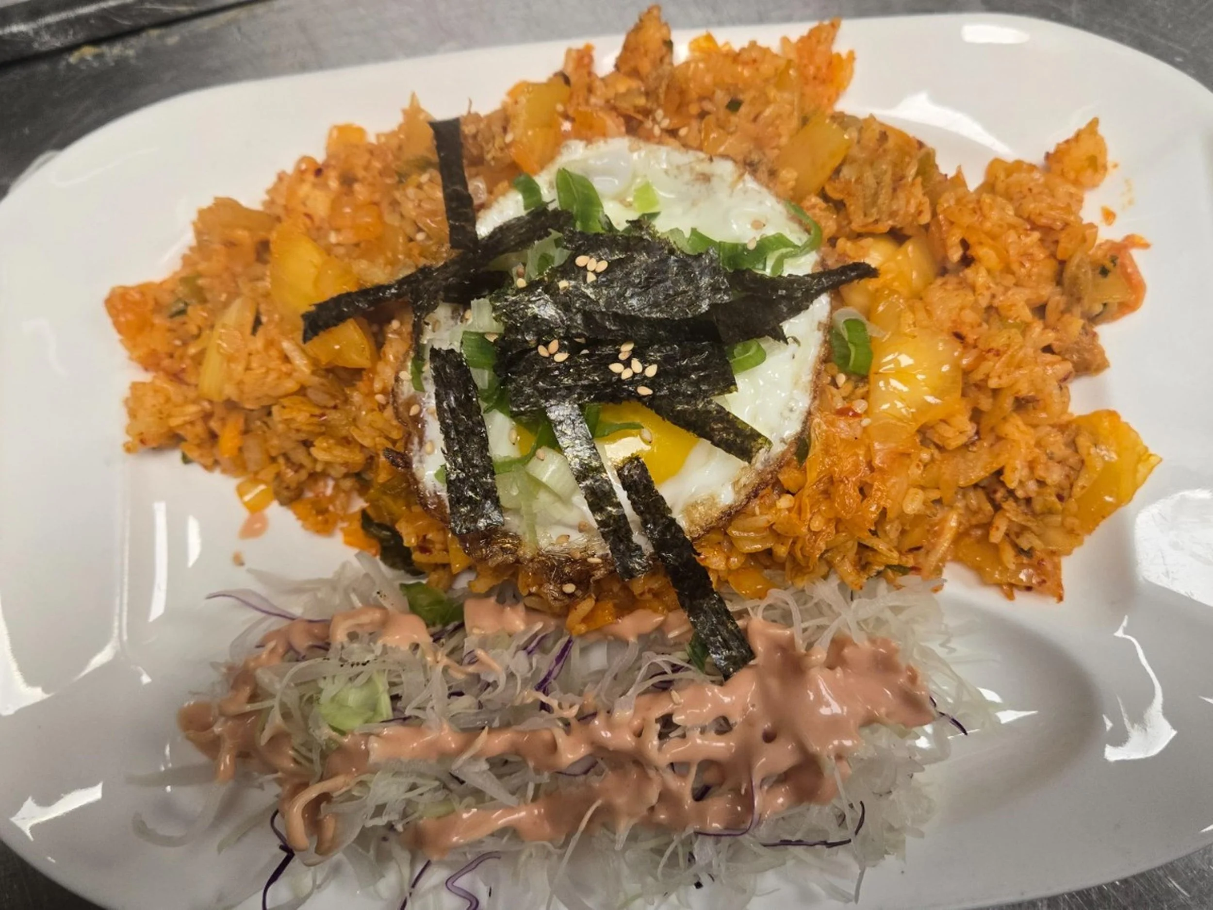 Plate of fried rice with shredded seaweed and green onions topped with a sunny side up egg, served with a side of shredded cabbage salad