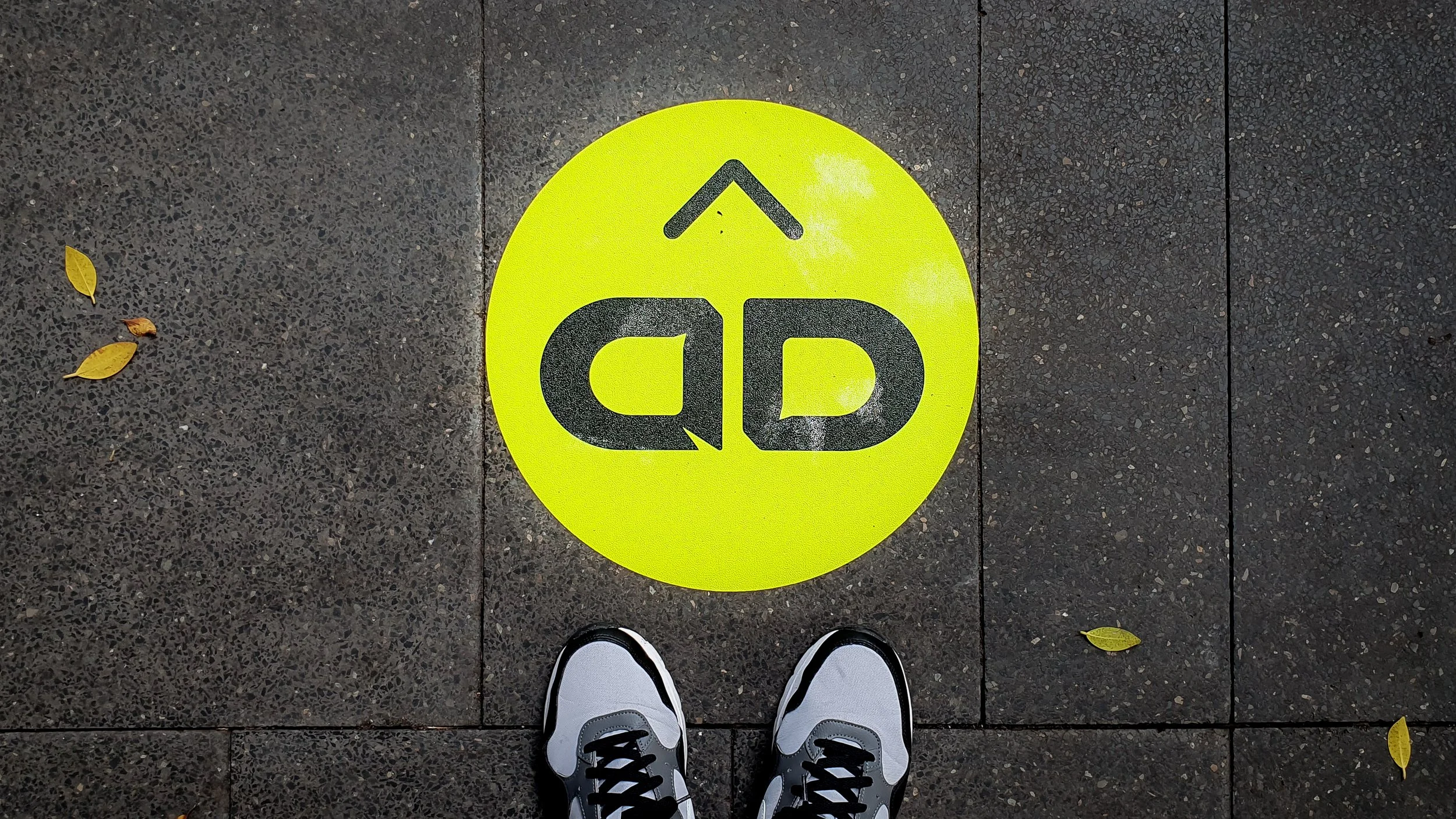 UNSW Art & Design Annual 2024 logo applied to a bright neon green circular sticker on a dark tiled surface.
