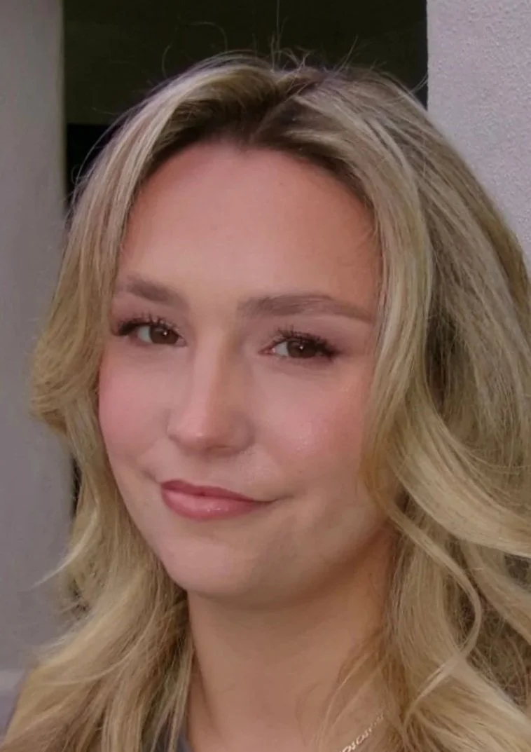 Close-up of a woman with wavy blonde hair smiling subtly