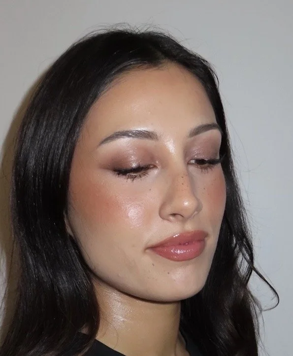 Close-up of a young woman with dark hair, light makeup, and closed eyes, against a light background.