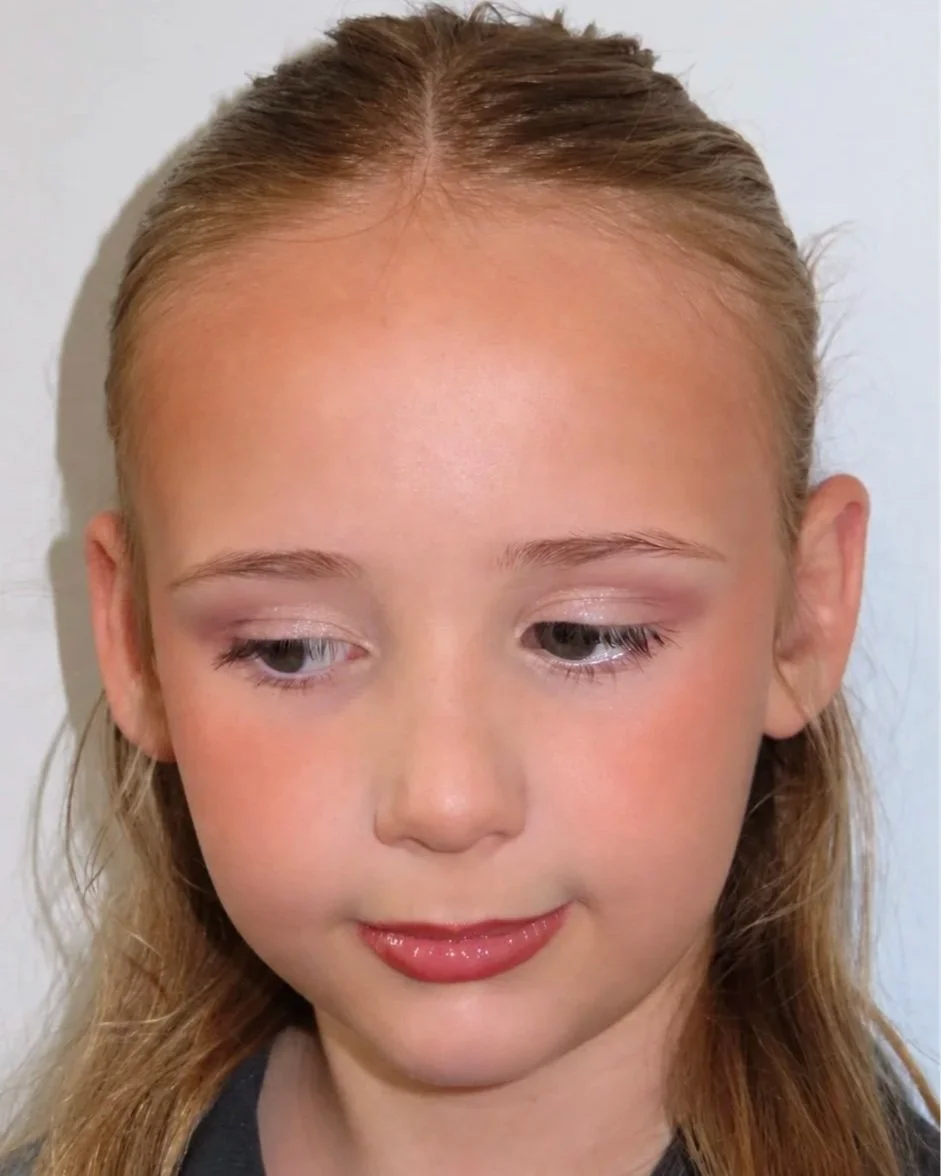 A young girl with blonde hair and light skin, looking down with a slight smile.