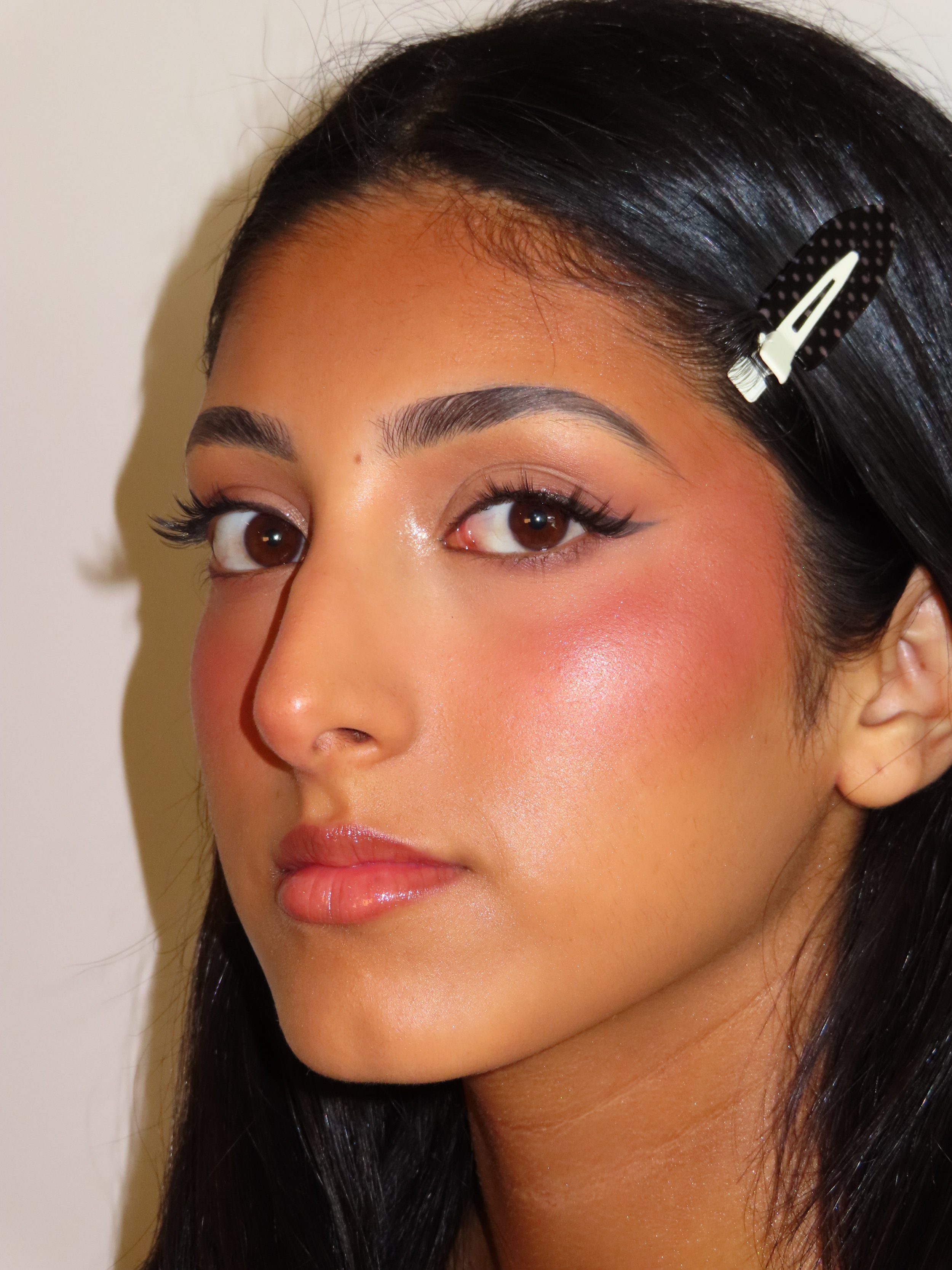 Close-up of a woman's face showing her eye makeup, eyebrow, and a hair clip securing her black hair.