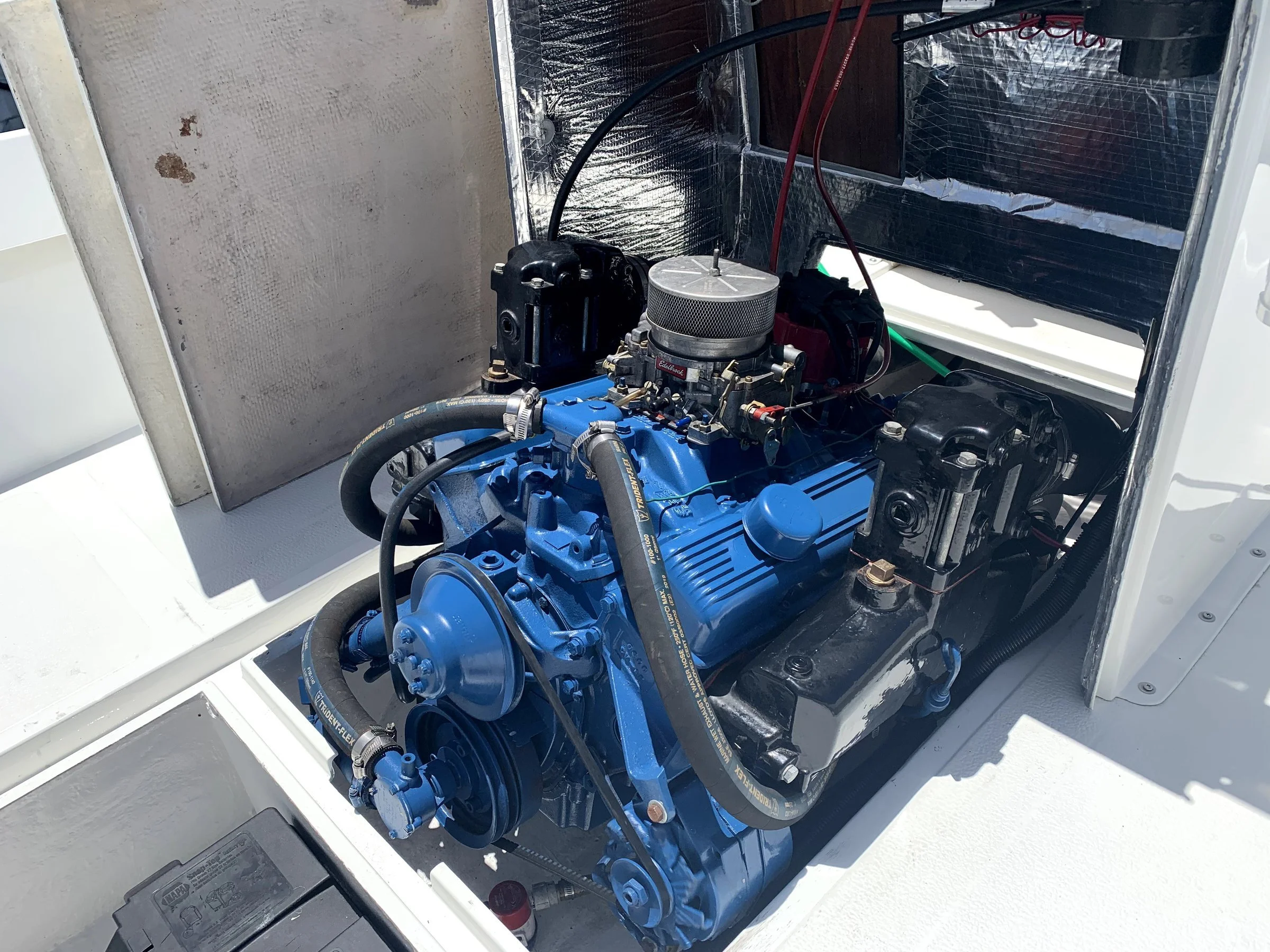 Close-up view of an engine inside a white enclosure, showing various mechanical and electrical components, including hoses, wires, and a metallic filter.