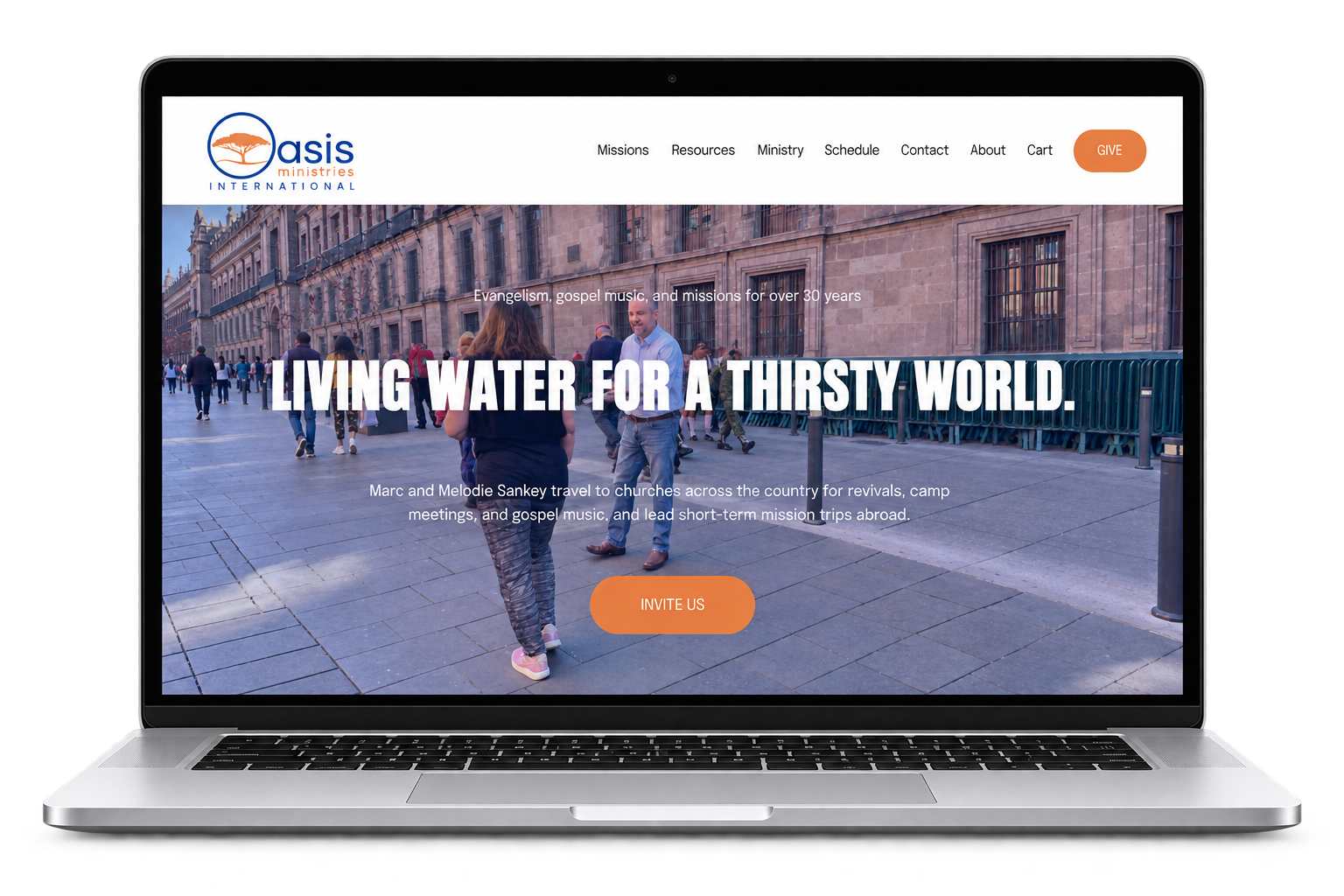 Laptop displaying the Oasis Ministries International website homepage with a city street photo and “Living Water for a Thirsty World” mission message.