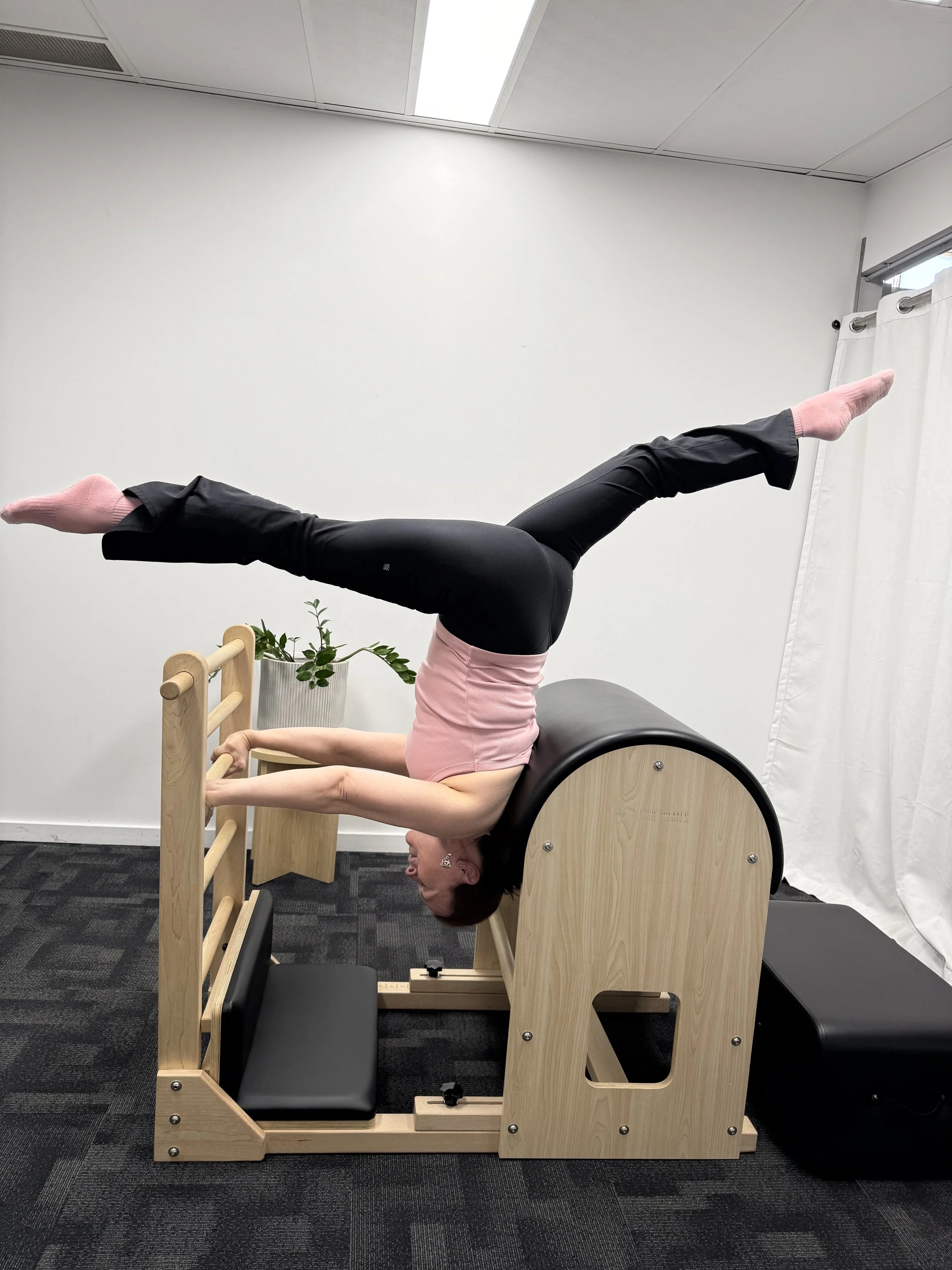 Person performing a headstand exercise on a Pilates reformer machine in a fitness studio.