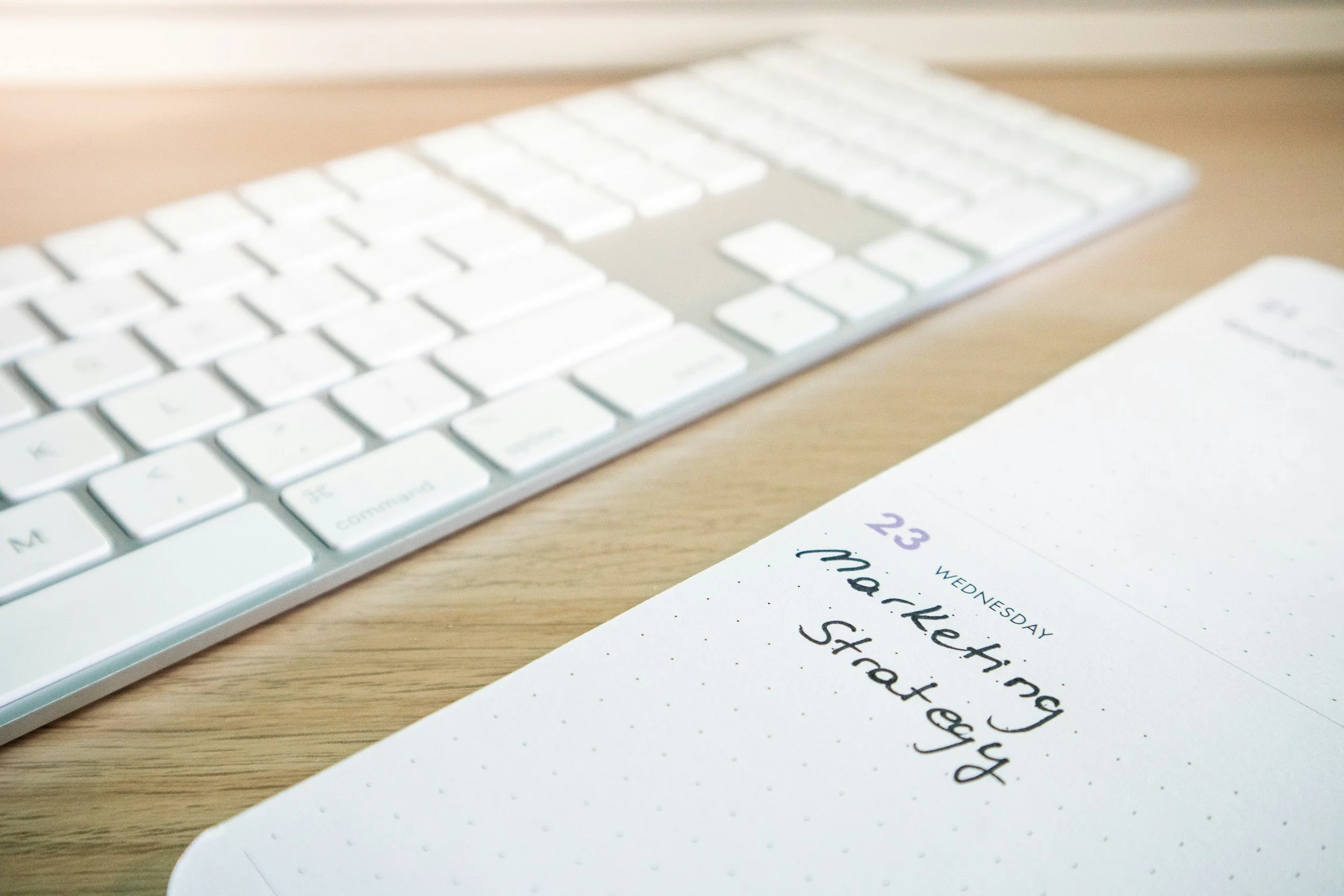 A white computer keyboard on a wooden desk with a piece of paper nearby containing handwritten notes.
