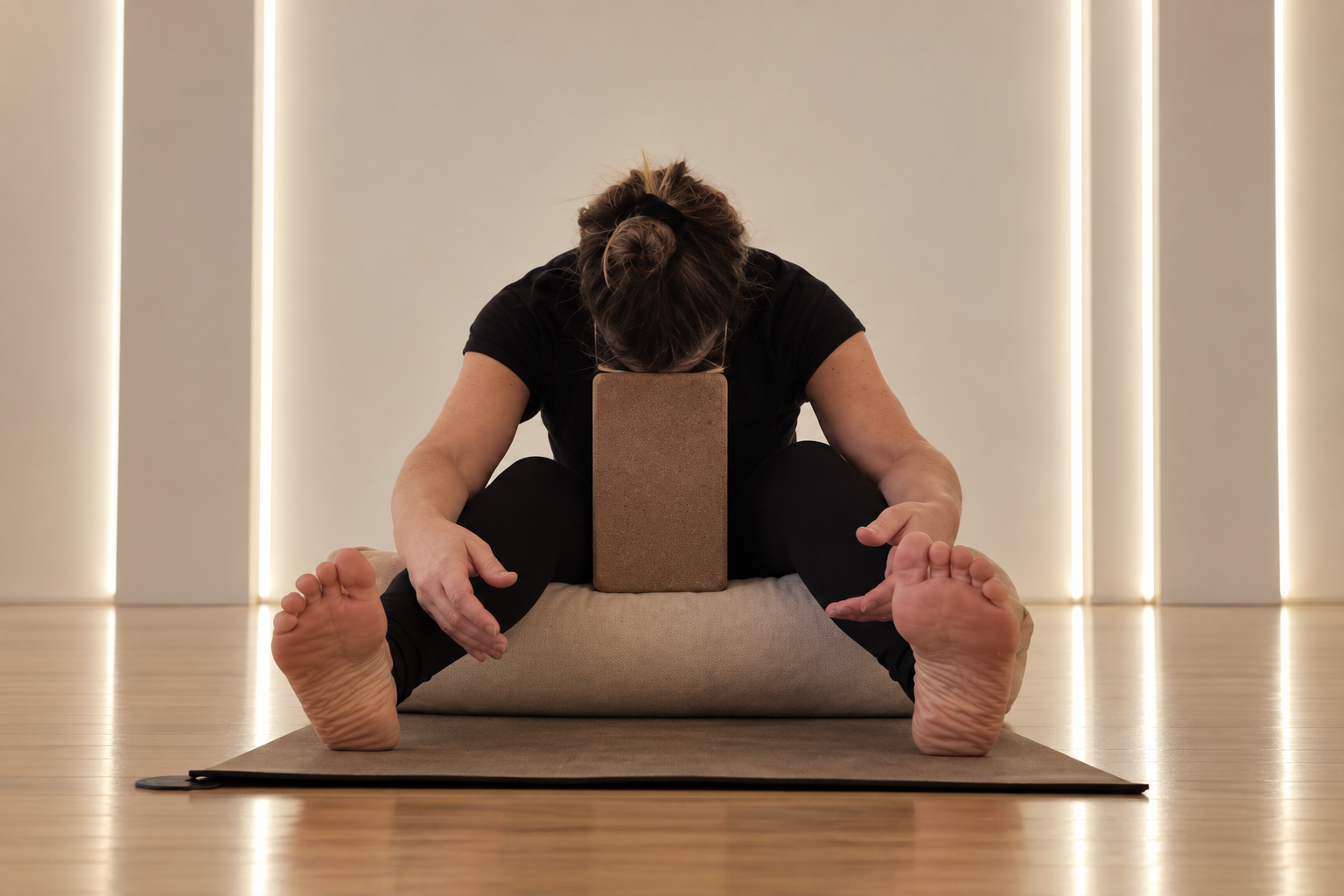 Erin Coffey seated on a yoga mat in a supported forward bend, with a bolster supporting her lower back and a block under her chest, at The Lady Osteo in Fyansford, Geelong.