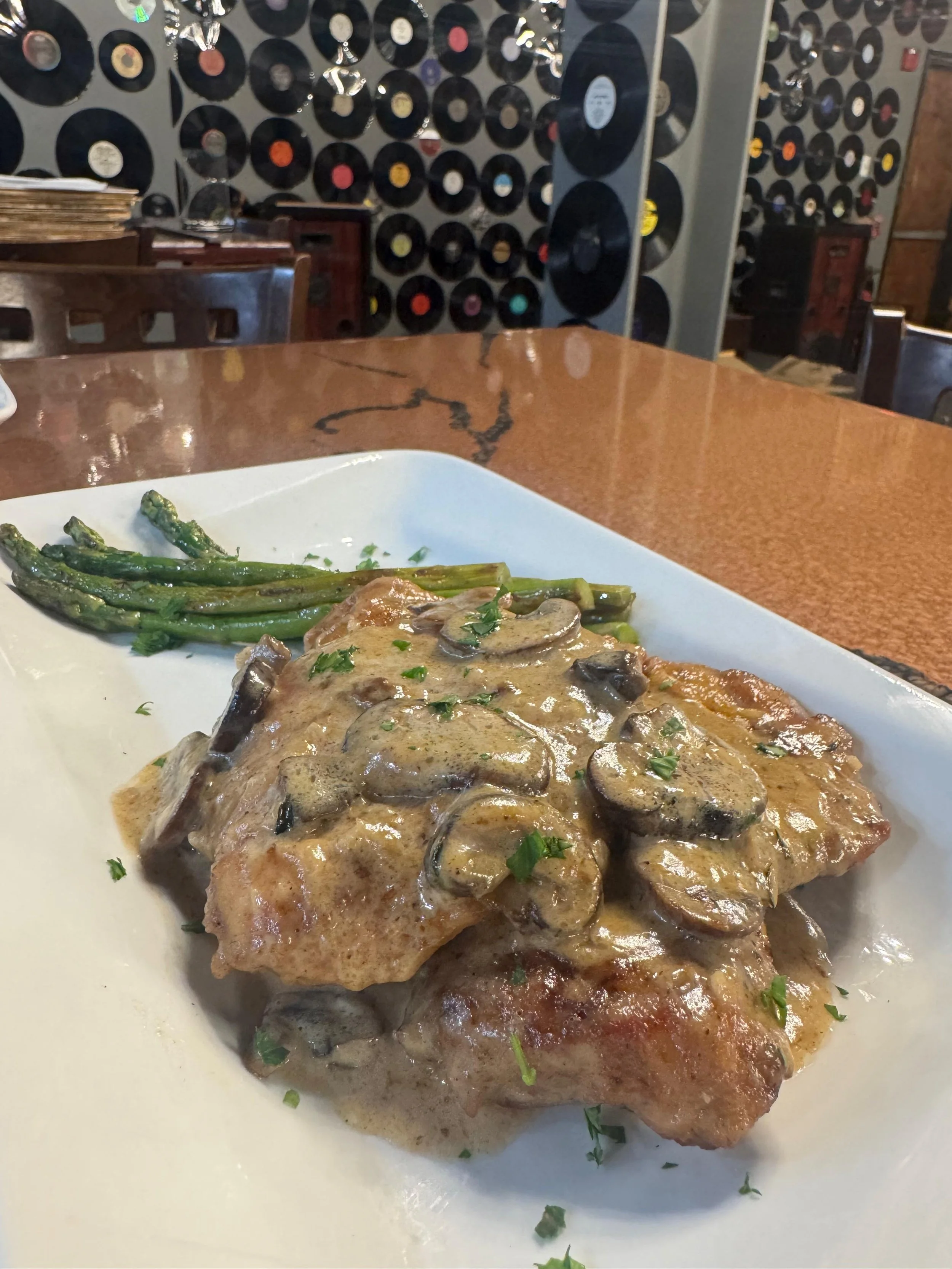 A plate of cooked fish topped with mushroom gravy and garnished with chopped herbs, accompanied by green asparagus spears.