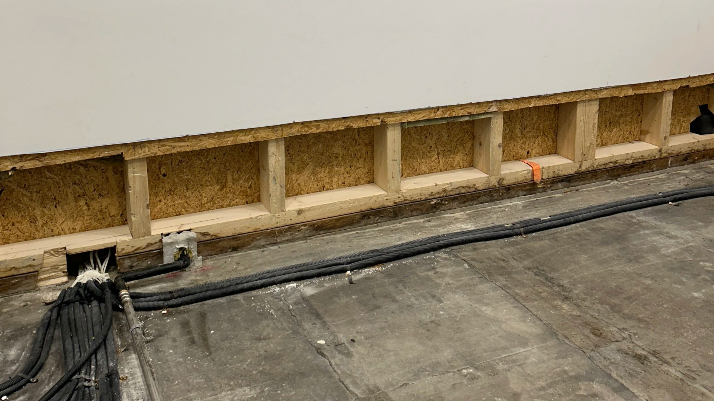 Baustelle mit freiliegender Holzrahmenwand, OSB-Platten und schwarzen Kabelschutzrohren auf dem Betonboden