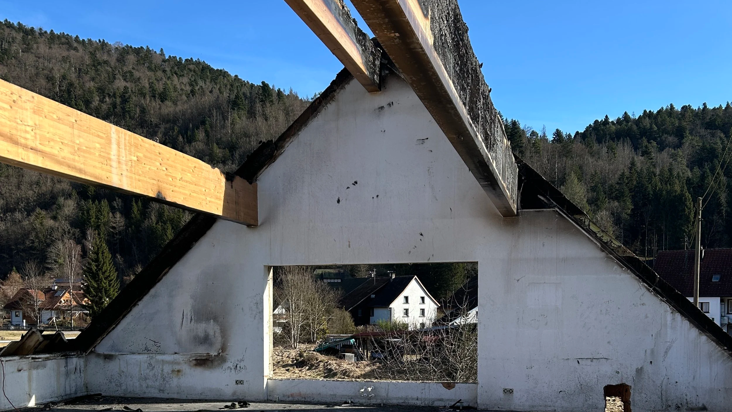 Abriss eines alten Hauses mit sichtbarer Holzdachkonstruktion vor bewaldeten Hügeln