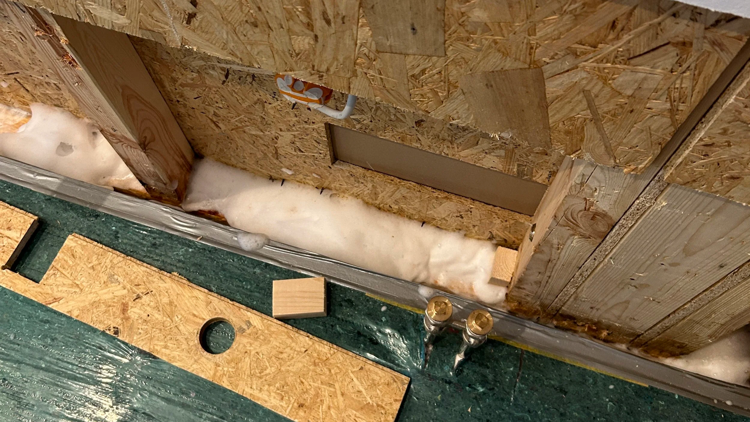 Offene Wand mit sichtbarer Dämmung, OSB-Platten, Wasserleitungen und einem elektrischen Anschluss.