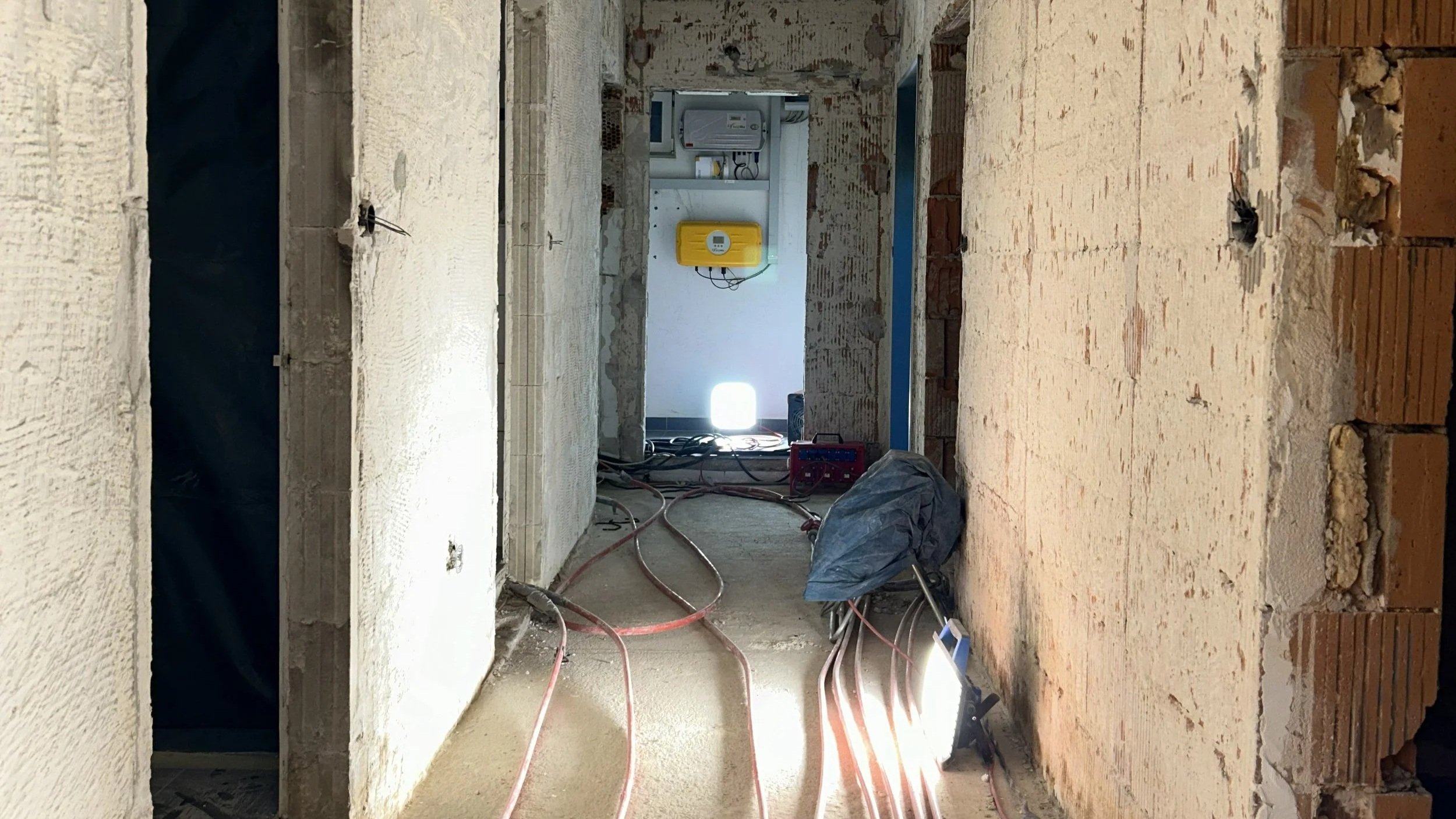 Baustelle in einem Rohbau mit freiliegenden Ziegelwänden, Kabeln, Schläuchen, Baustrahlern und Elektrogeräten