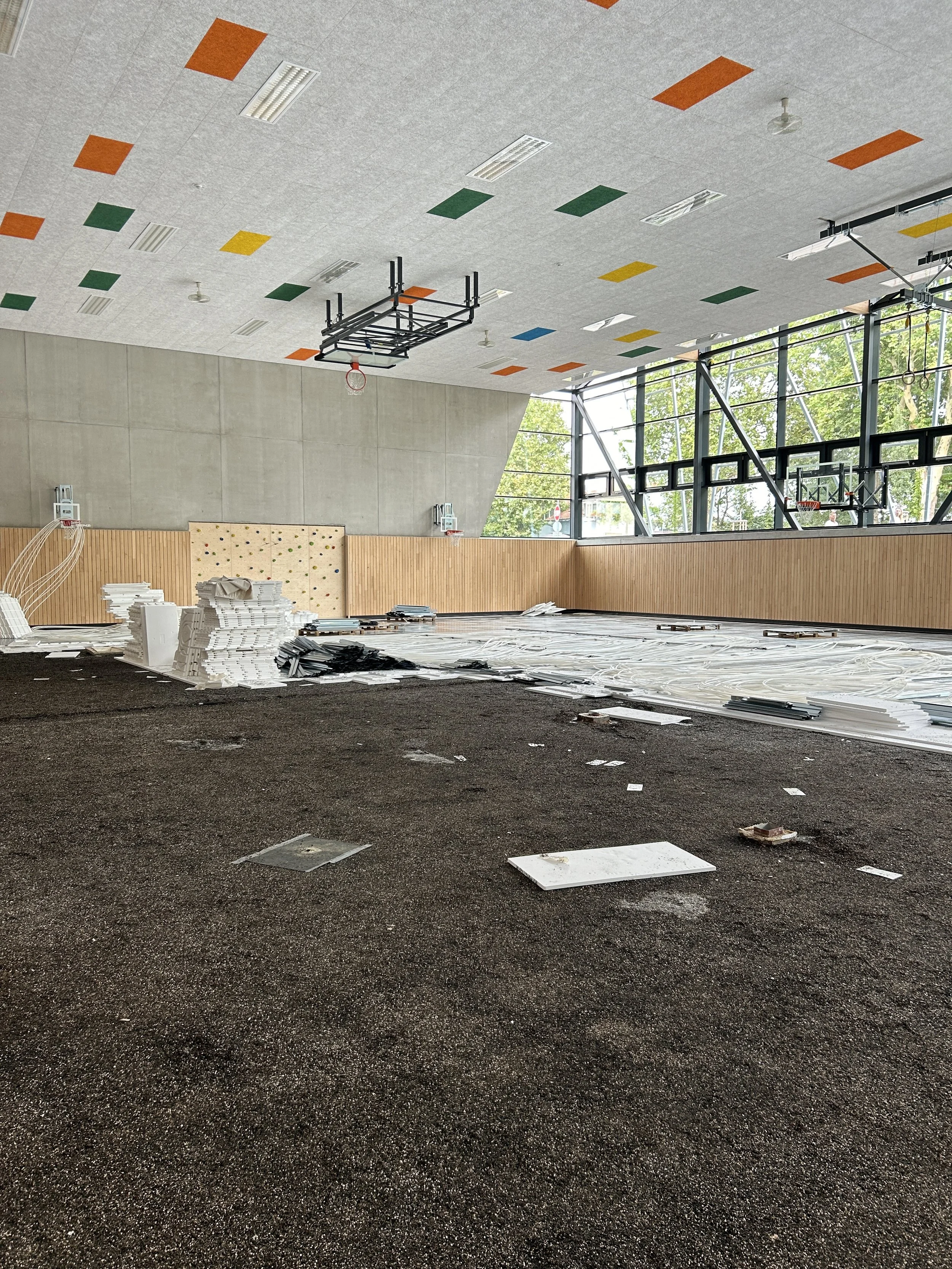 Sporthalle im Umbau mit Basketballkörben, Kletterwand, farbigen Akustikplatten und Baumaterial auf dem Boden
