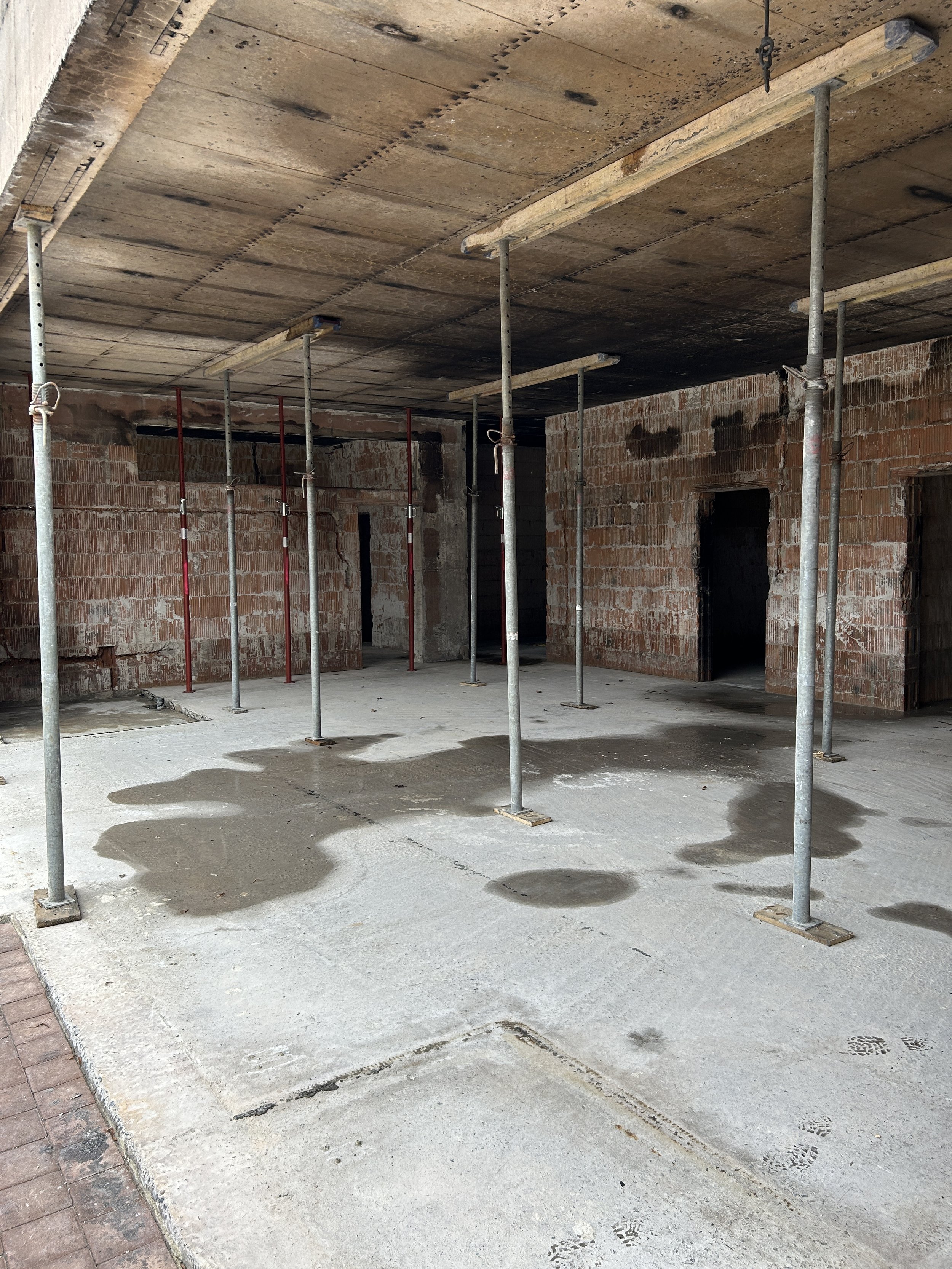 Rohbau mit unverputzten Ziegelwänden, Betondecke und zahlreichen Baustützen.