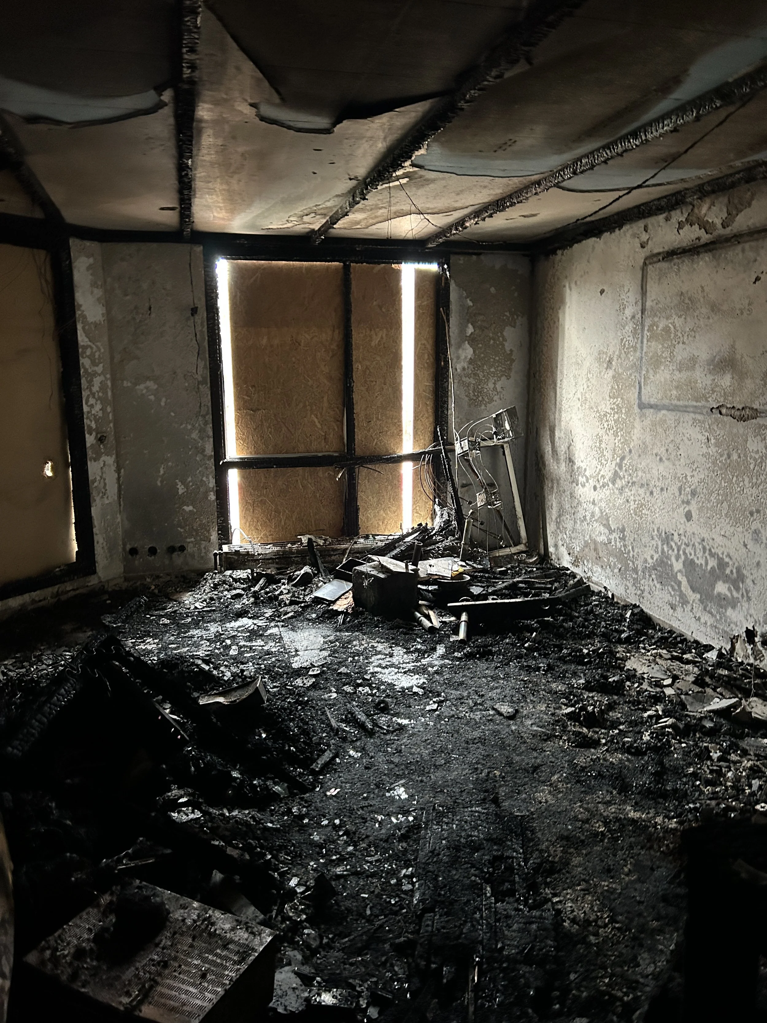 Ausgebrannter Innenraum mit verrußten Wänden, zerstörter Decke, verkohltem Boden und Brandschutt.
