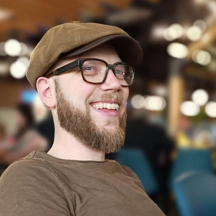 Lächelnder Mann mit Bart, Brille und Schiebermütze in einem Café