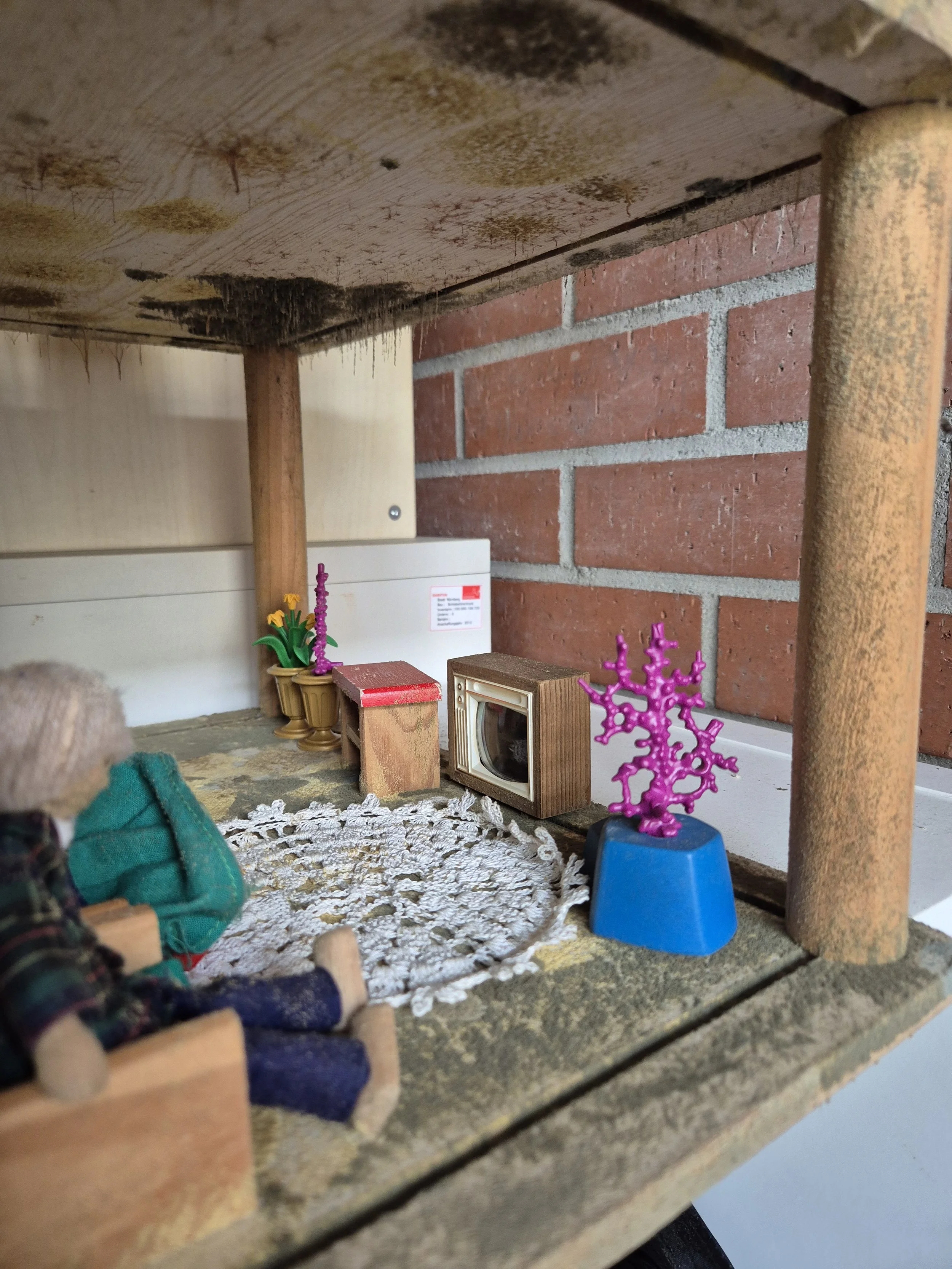Nahaufnahme eines rustikalen Tisches mit Puppen, bunten Dekorationen, Häkeldeckchen und einer Backsteinwand im Hintergrund.