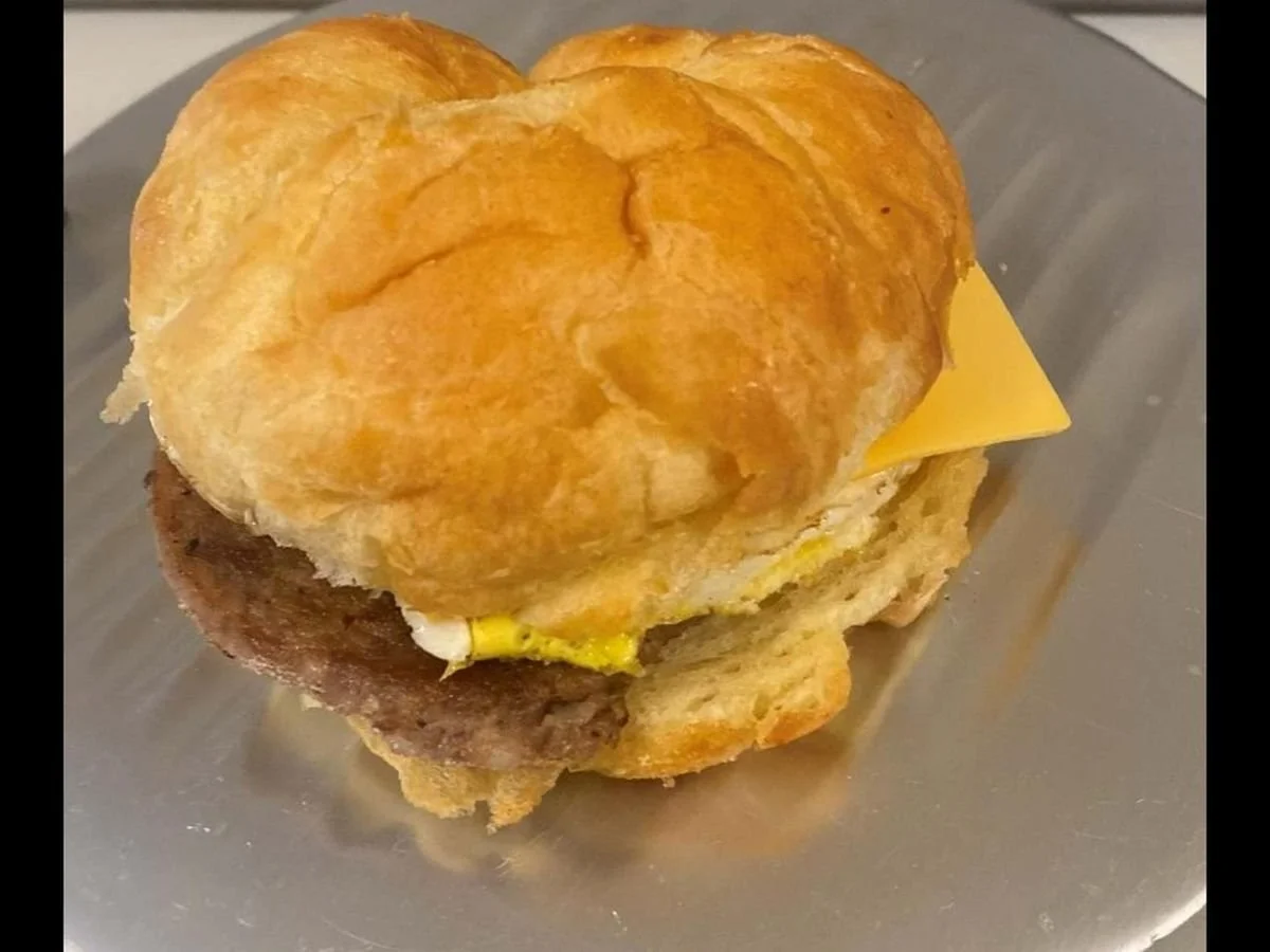 A breakfast sandwich with a sausage patty, scrambled eggs, and a slice of cheese inside a croissant.