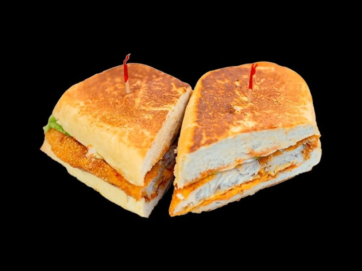 Half of a sandwich with fried chicken, lettuce, and mayonnaise, and the other half with turkey and cheese, both with lit birthday candles, on a black background.
