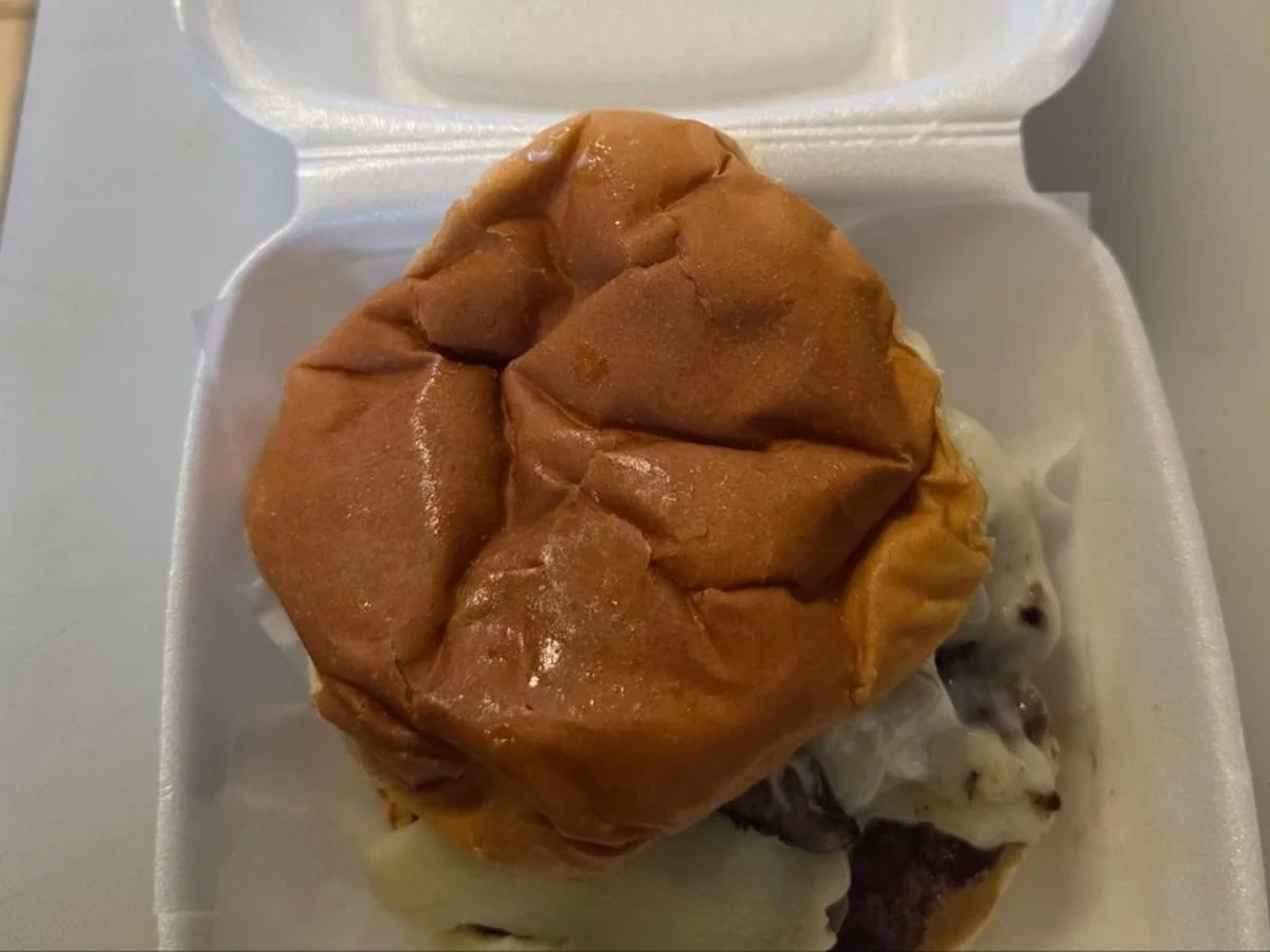 A cheeseburger with a toasted bun in a white foam container.