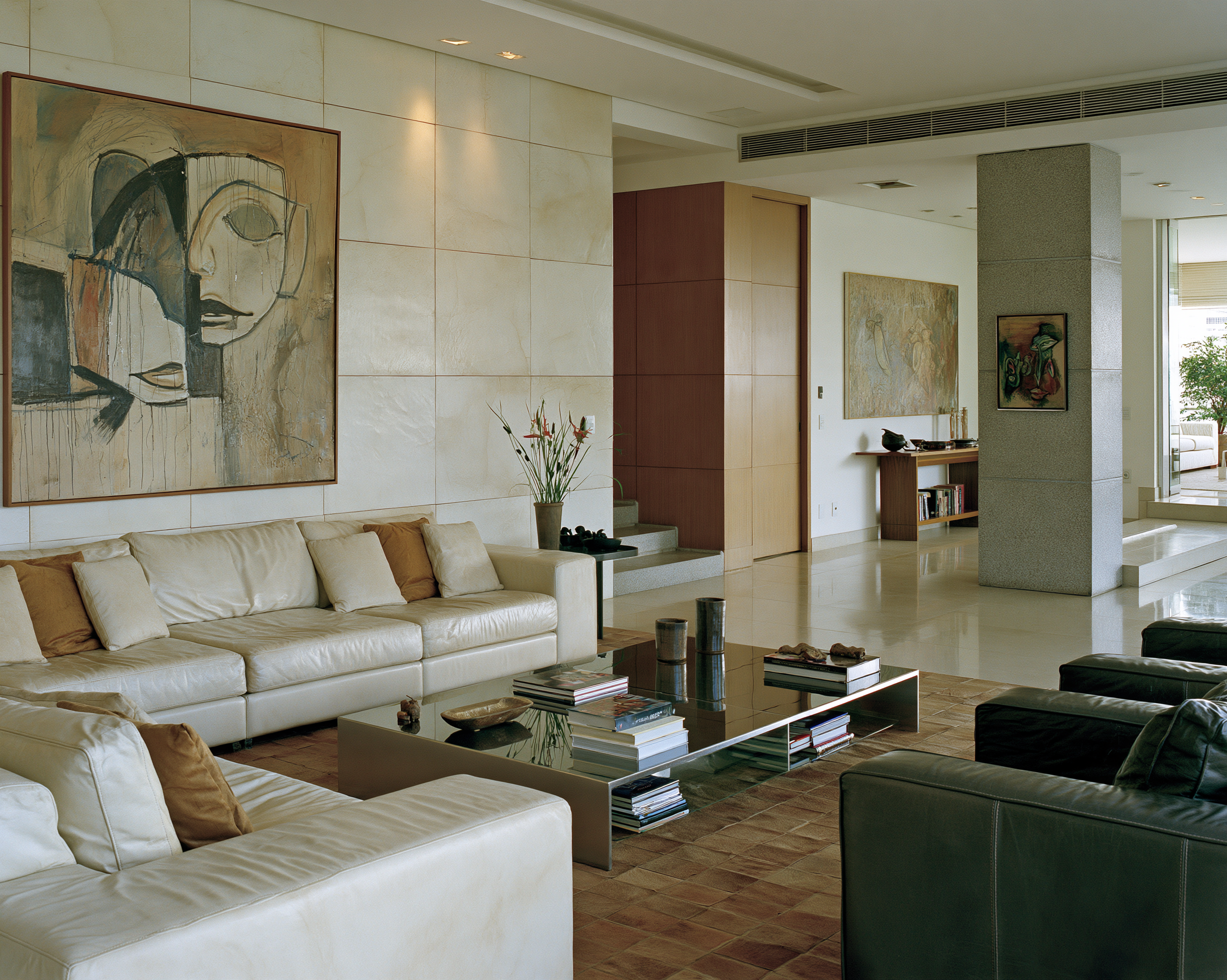 Ein elegantes, modern eingerichtetes Büro mit großen Fenstern, Blick nach draußen auf Bäume, mit einem Schreibtisch, einem Bürostuhl, Sofas und Regalen mit Büchern und Dekorationsgegenständen.