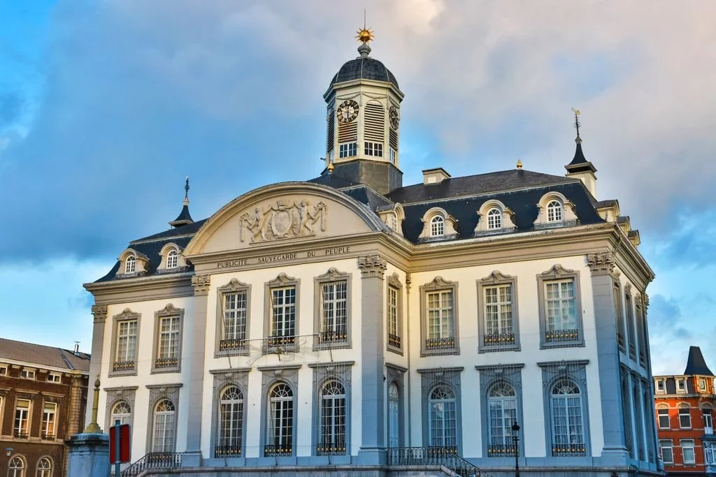 Bâtiment historique blanc avec un dôme au sommet, situé dans un paysage urbain, ciel partiellement nuageux.