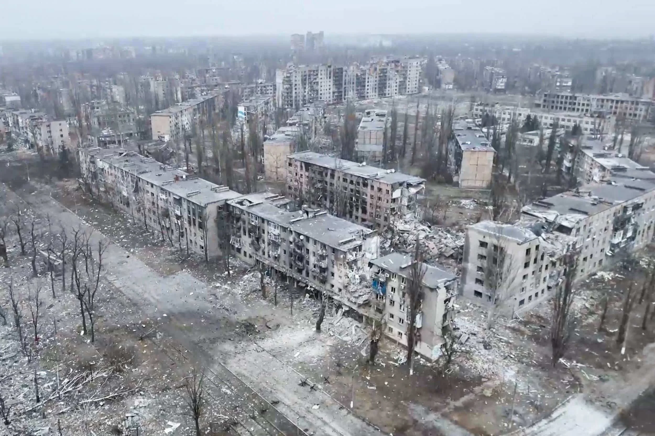 Vues d'une ville avec de grands immeubles résidentiels, certains endommagés, et des débris au sol, suggérant des dégâts ou un conflit.