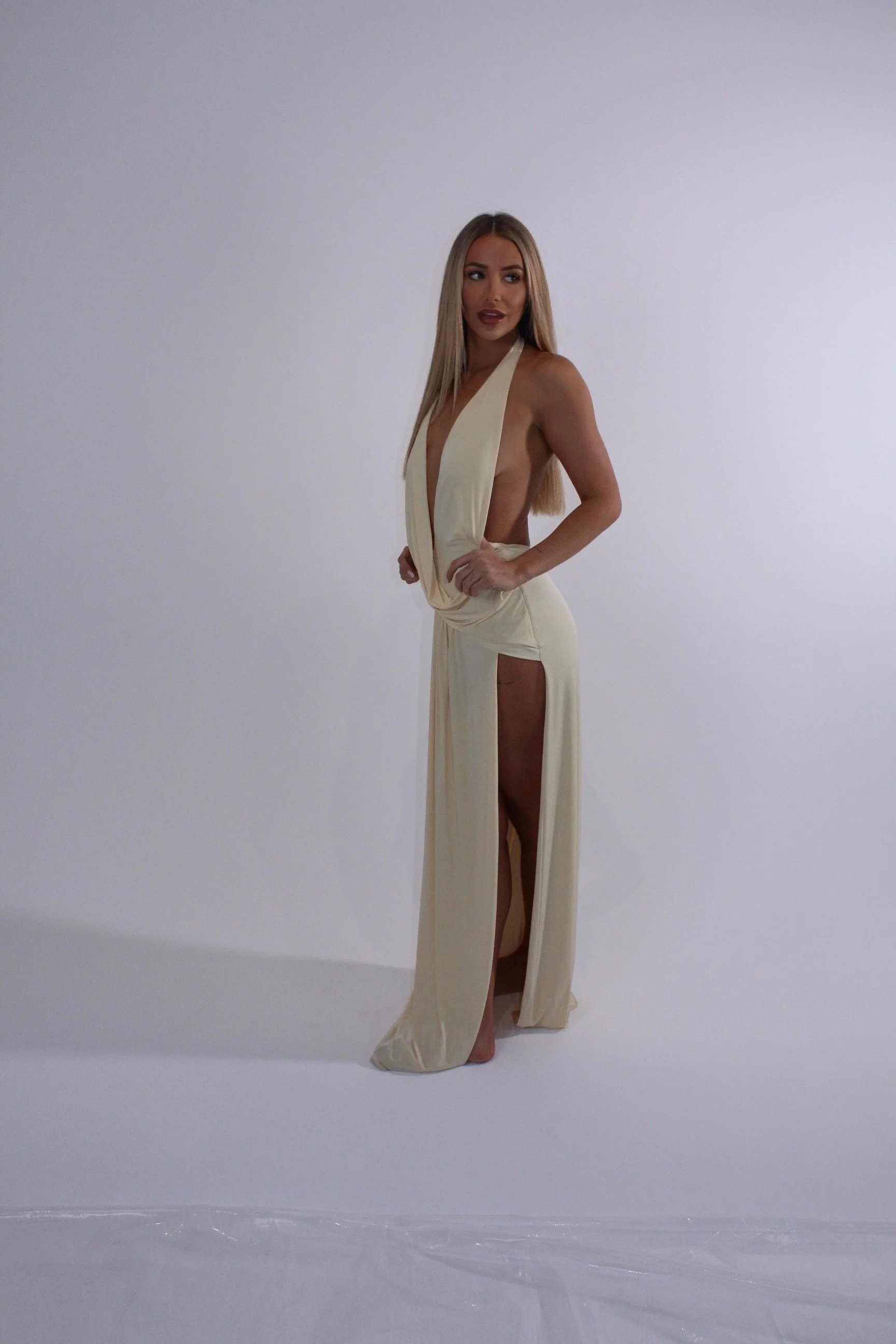 Blonde model posing in a cream cutout halter gown against a white studio backdrop