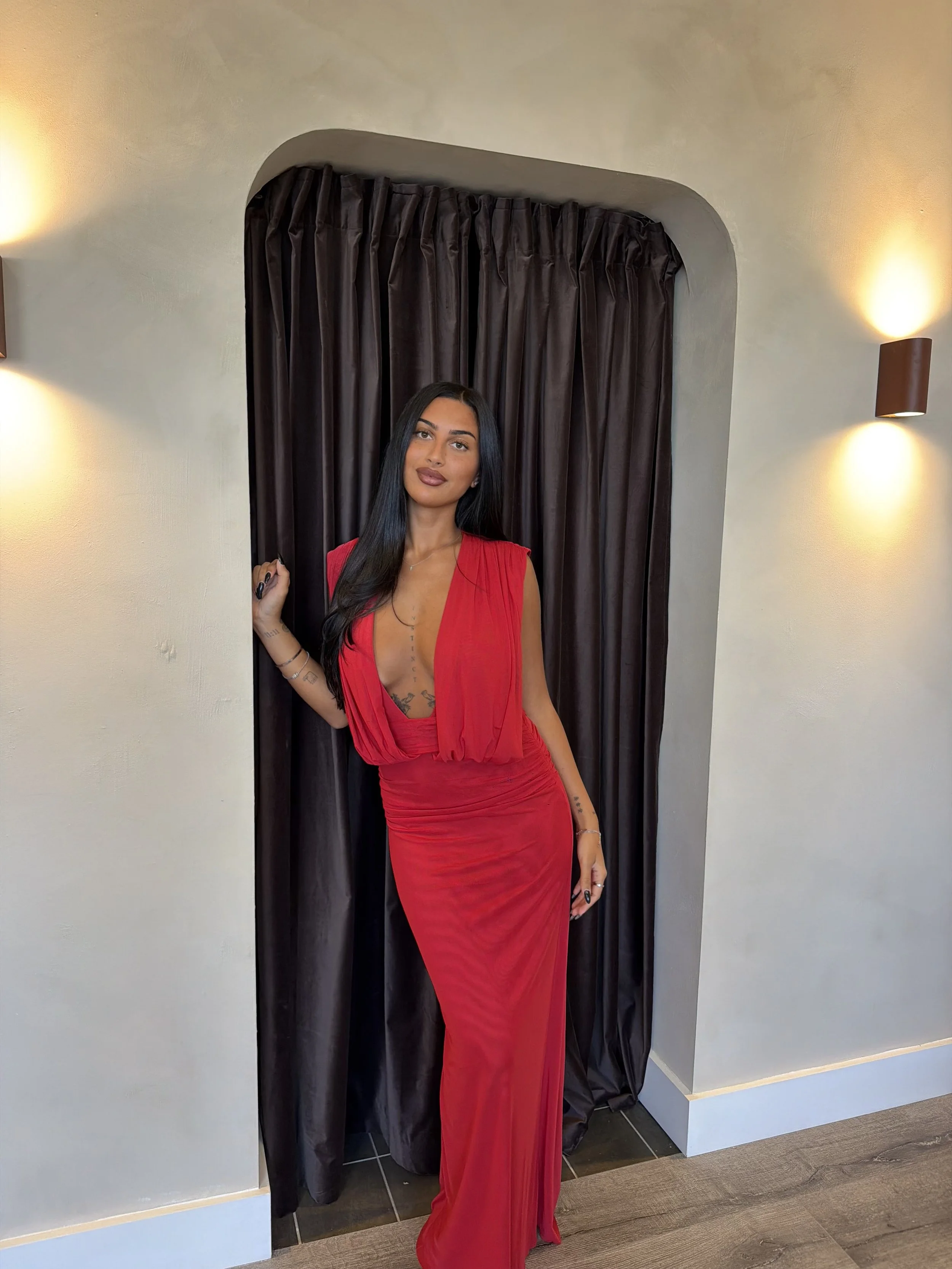 Woman in a red dress posing in front of black curtains and wall sconces