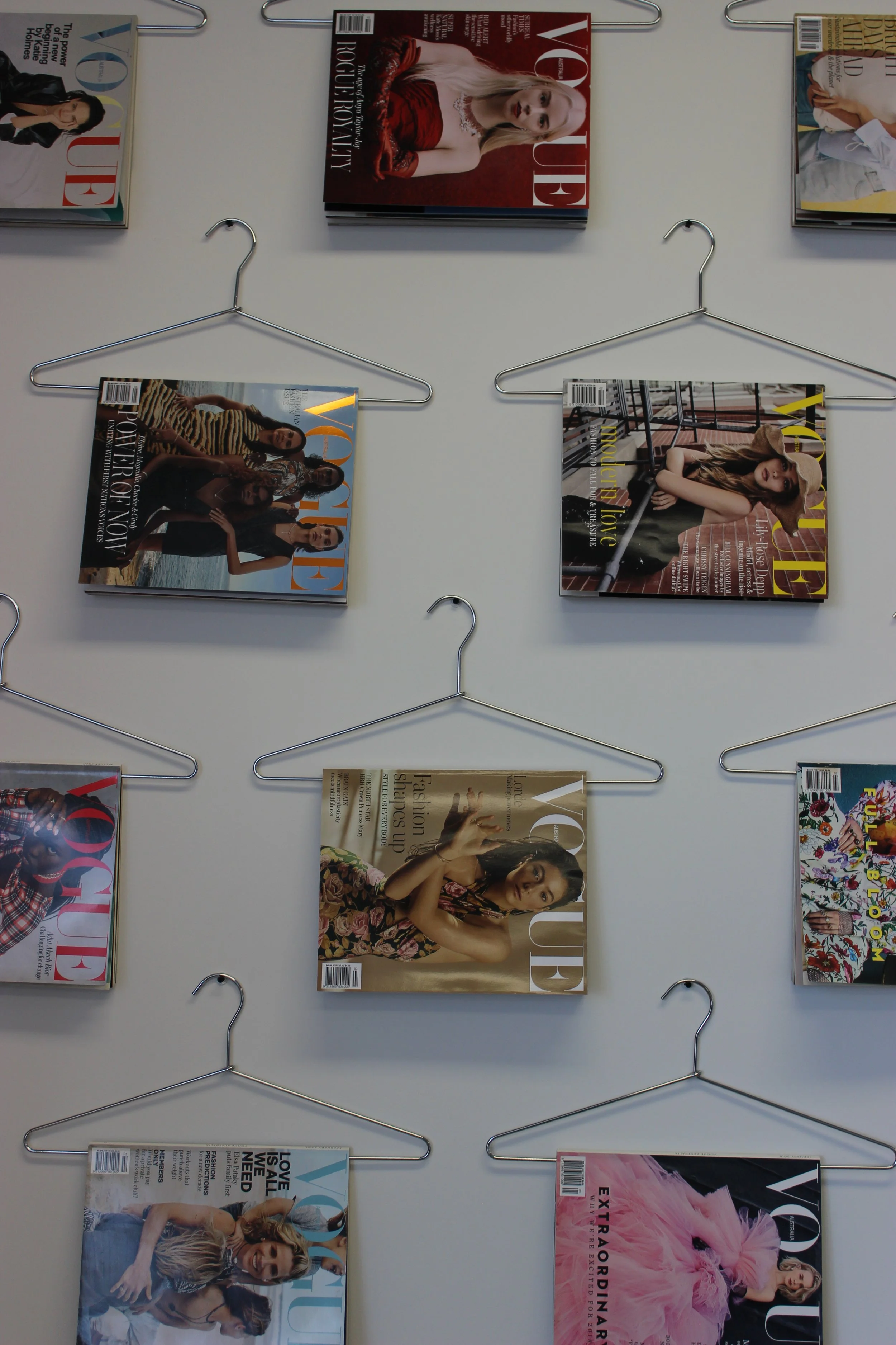 Grid of Australian Vogue magazine covers displayed on metal wire hangers against a wall.