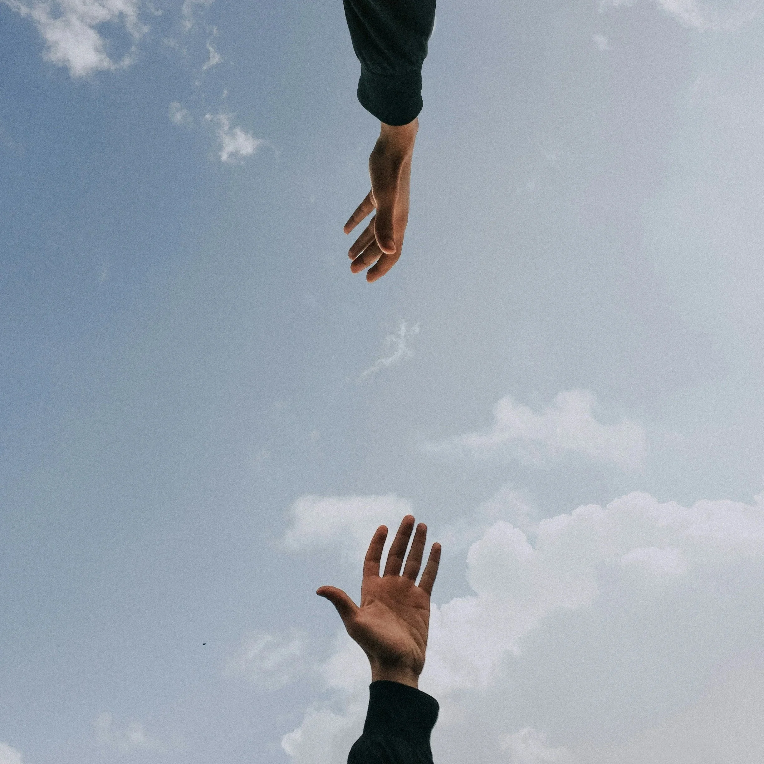 A person's hand reaching towards the sky with a background of blue sky and scattered clouds.