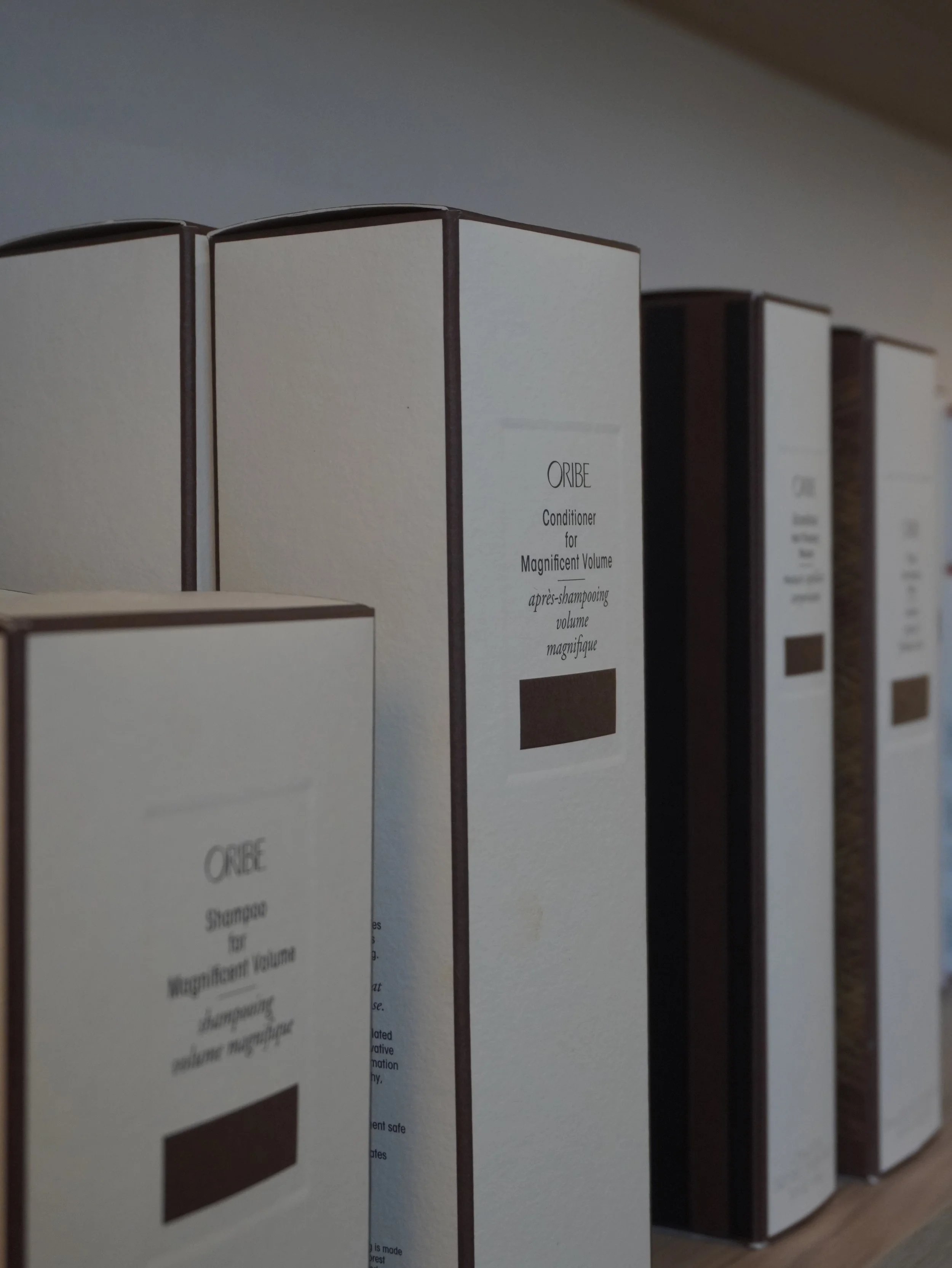 Close-up of white packaging boxes for Oribe conditioner and shampoo on a shelf.