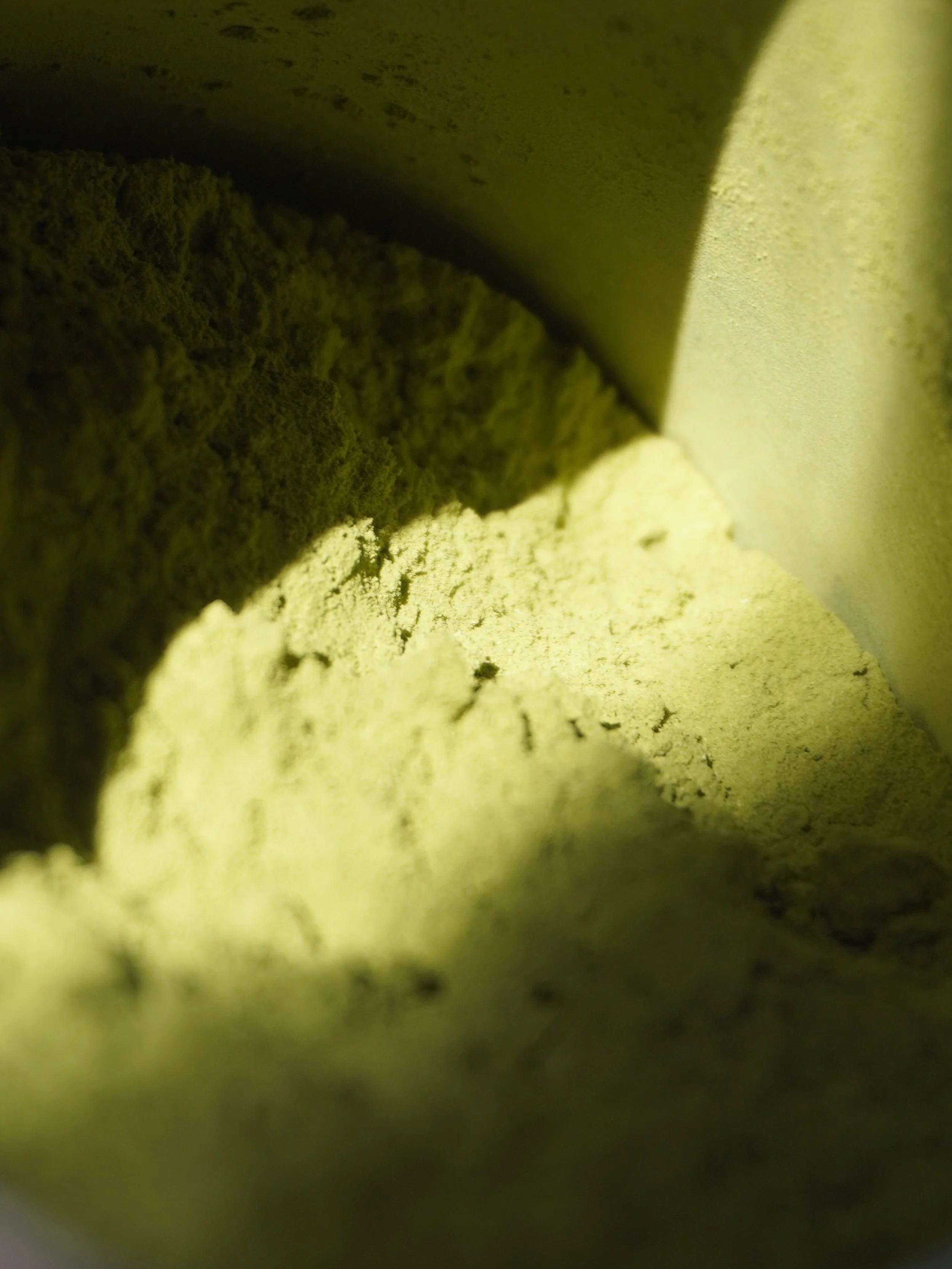 Close-up of a greenish, textured surface with a shadowed edge and faint darker spots, possibly a wall or a piece of fabric.