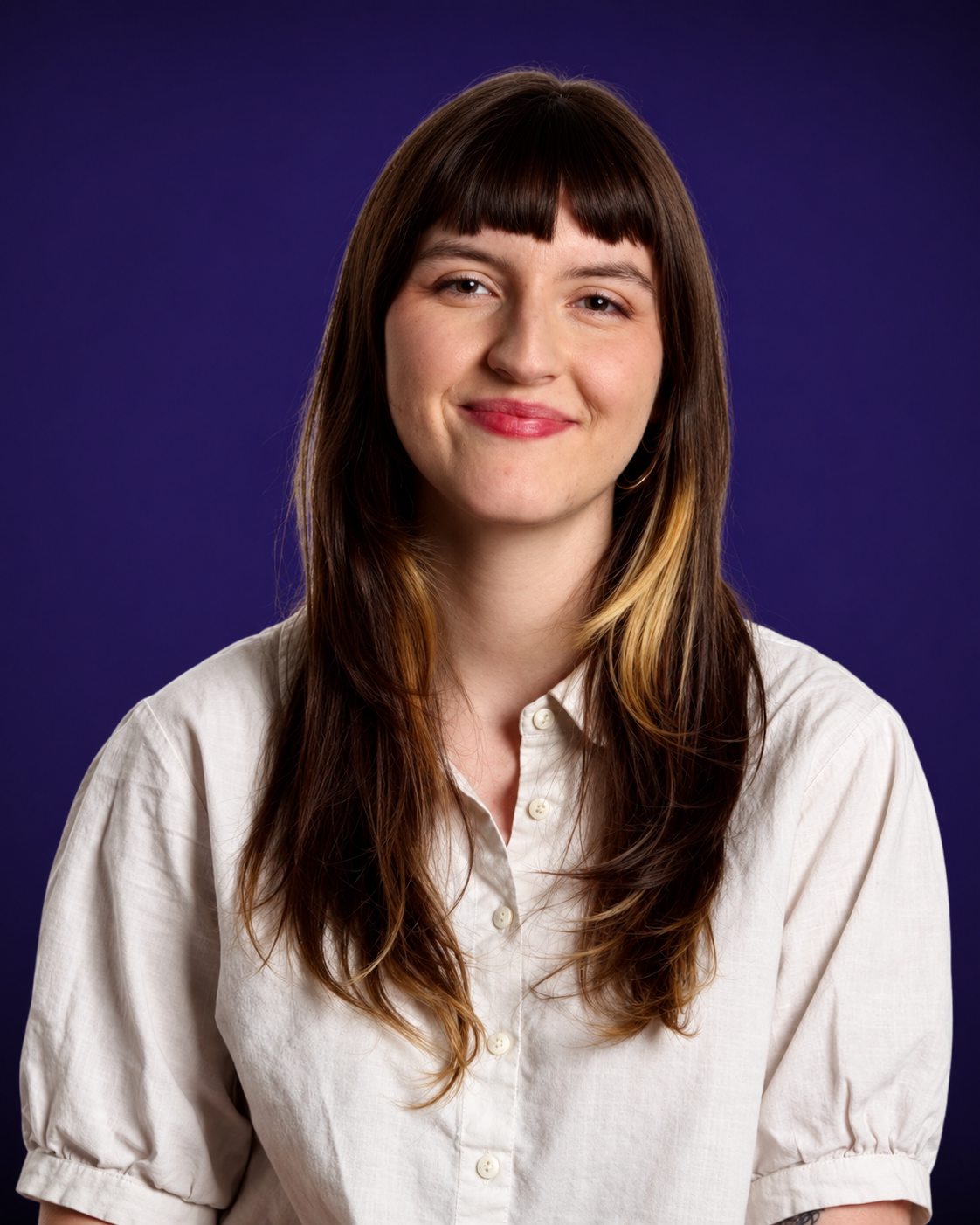 Portrait of a woman with brown hair and blonde highlights, wearing a white button-up shirt, smiling, against a purple background.