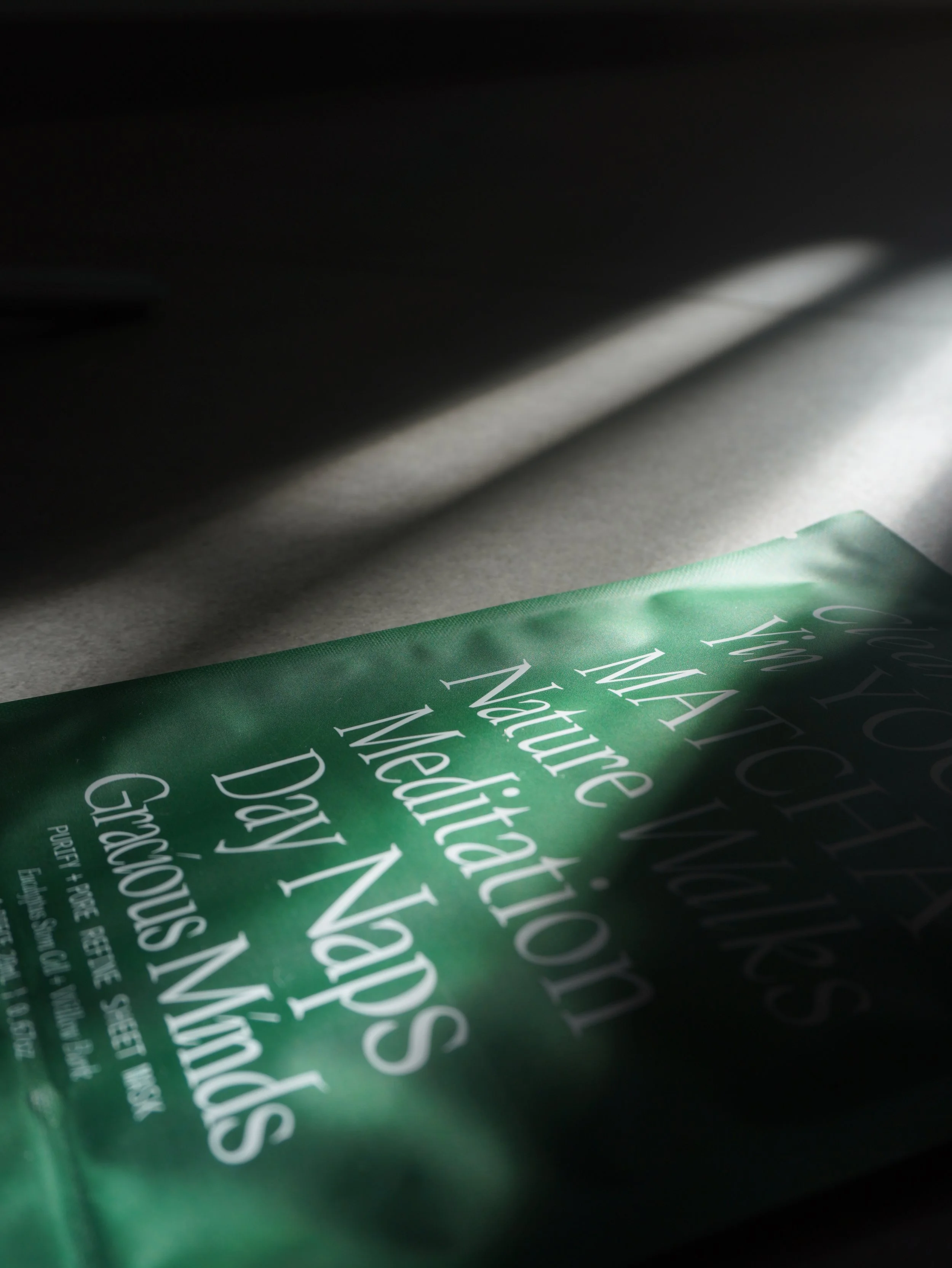 Close-up of a green package with white text, under a shadow, with a focus on the word 'Natural'.