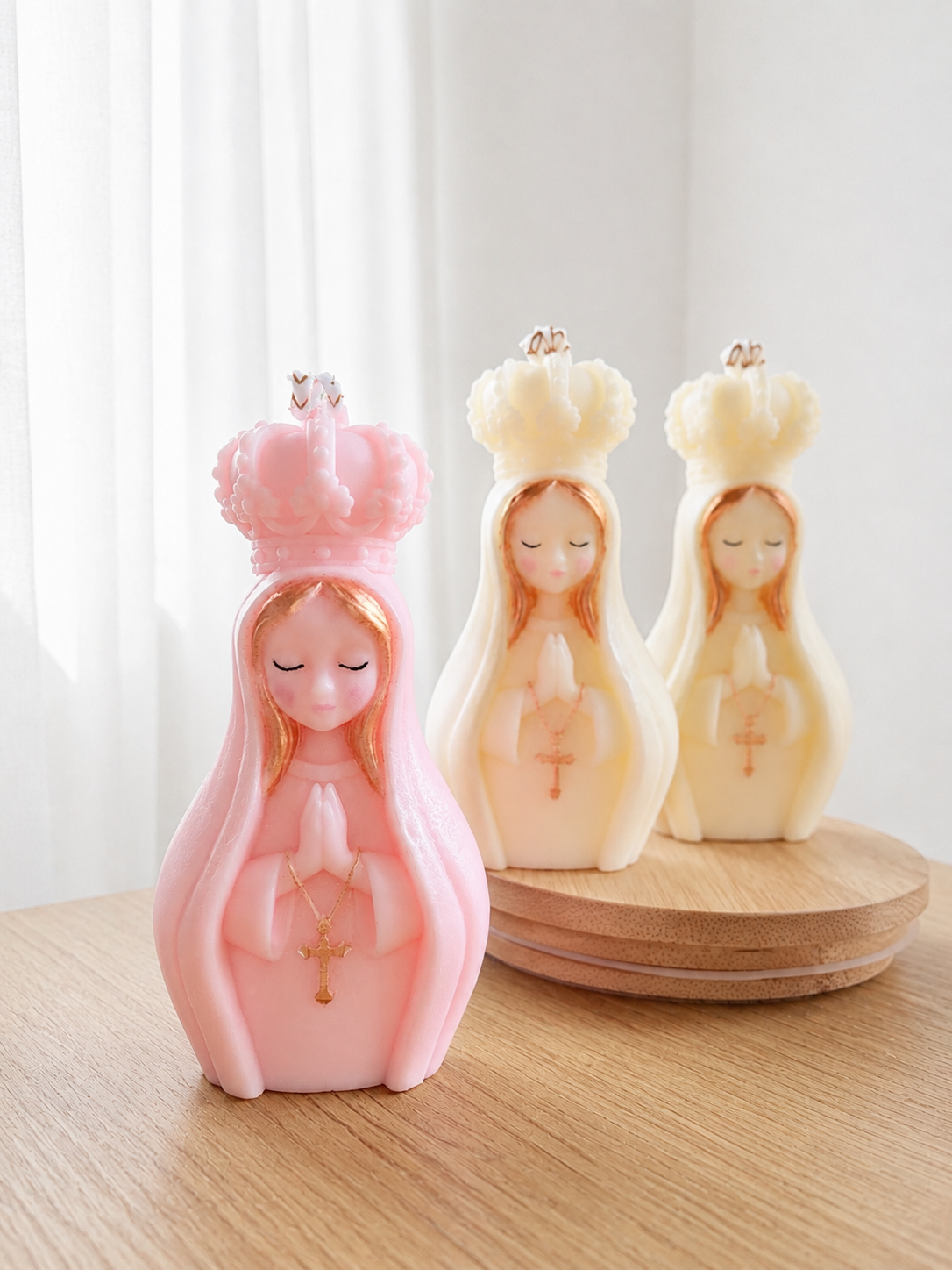 Figuras decorativas de vírgenes con coronas y rosarios, colocadas en una mesa de madera y en un plato de madera.