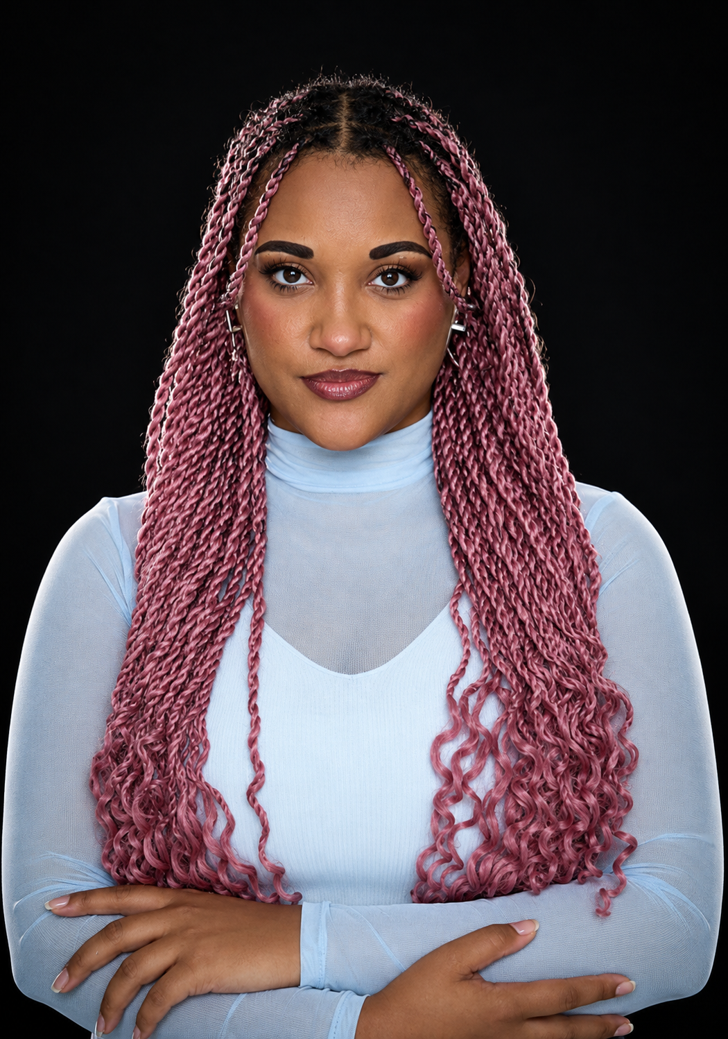 A woman with long pink twists wearing a light blue sheer long sleeve top against a black background.