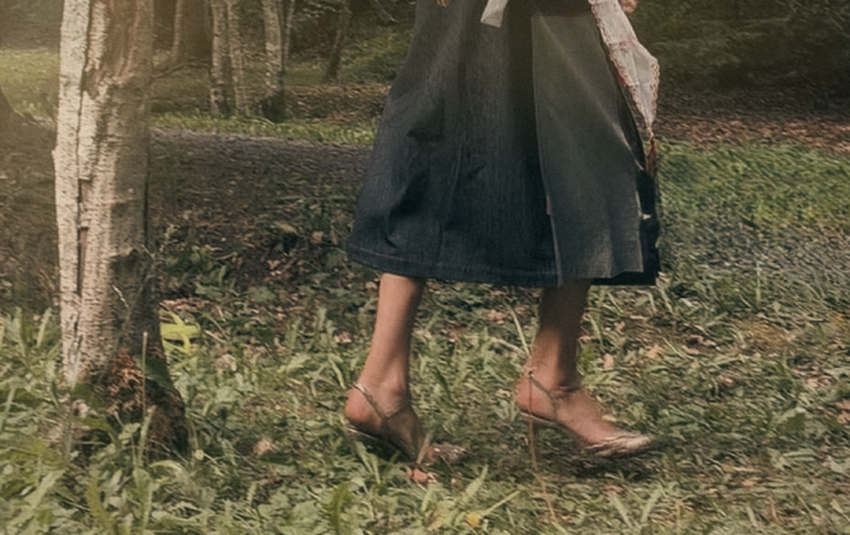 A person walking outdoors in a woodland area, wearing a denim skirt and high-heeled shoes. Beautiful legs.
