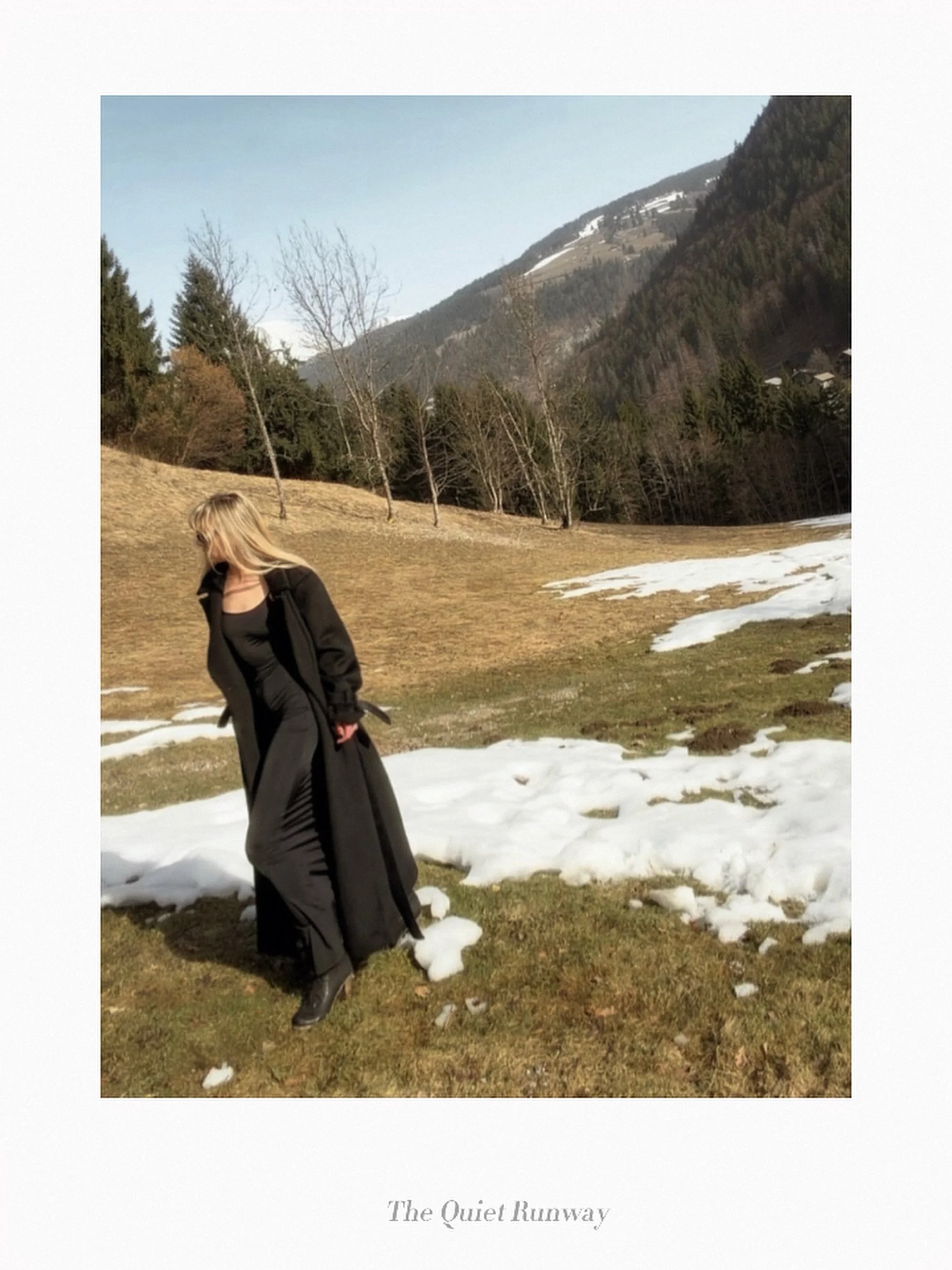 A woman in a black coat and boots walking on a grassy field with patches of snow, mountains in the background, and a partly cloudy sky, titled "The Quiet Runway."