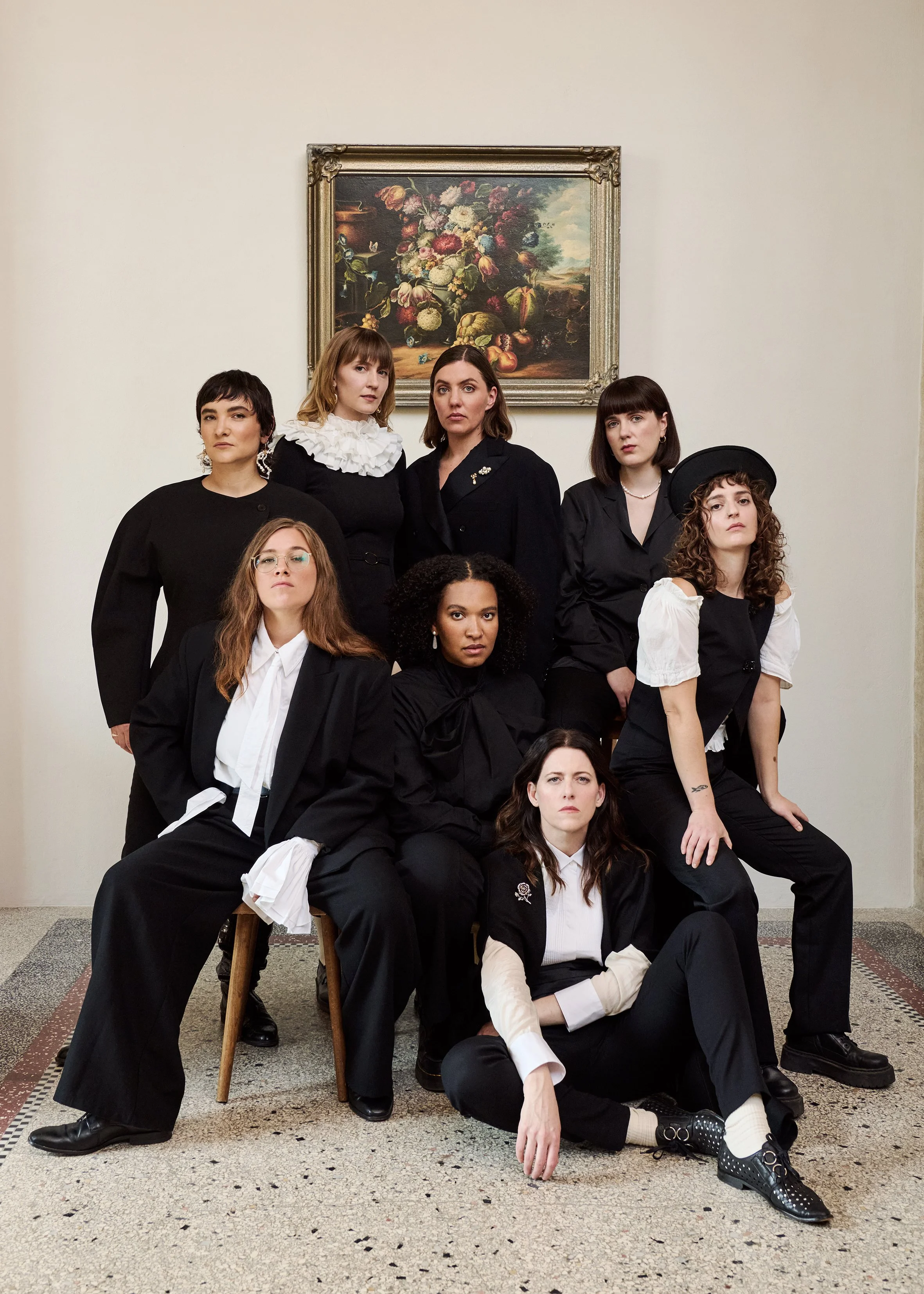 Group of eight women posing in front of a classical painting of flowers in an art gallery or museum.