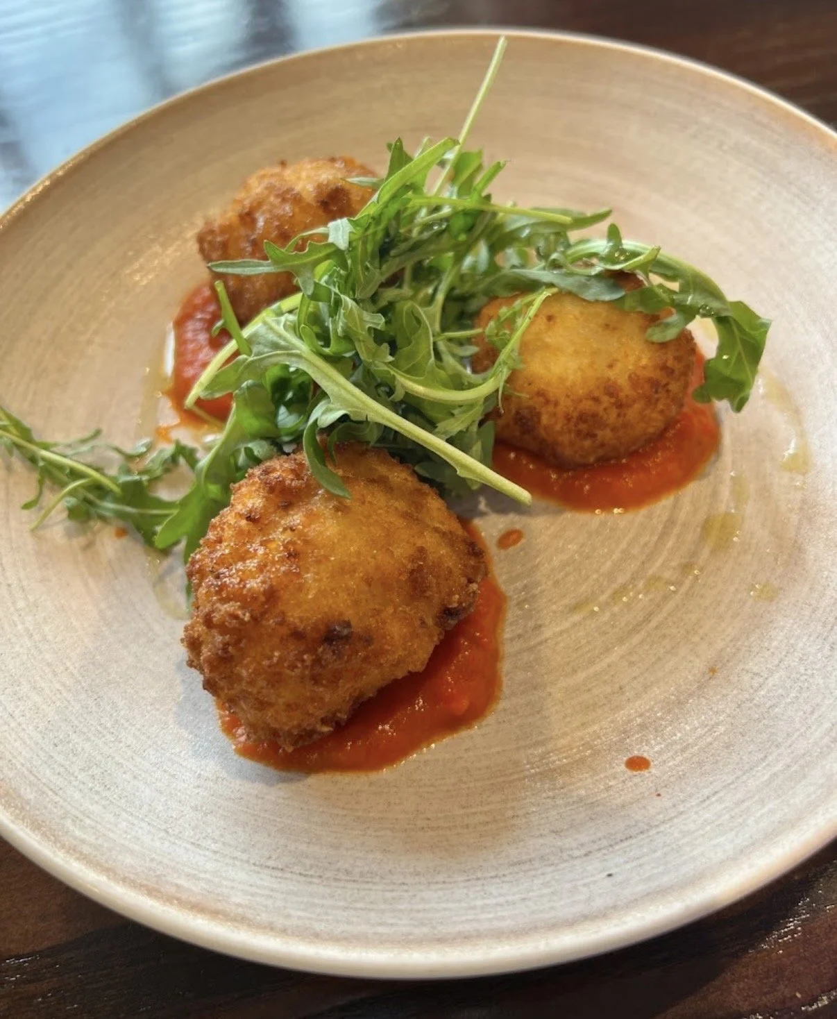 Fried cheese balls topped with fresh arugula on a bed of tomato sauce in a beige bowl.
